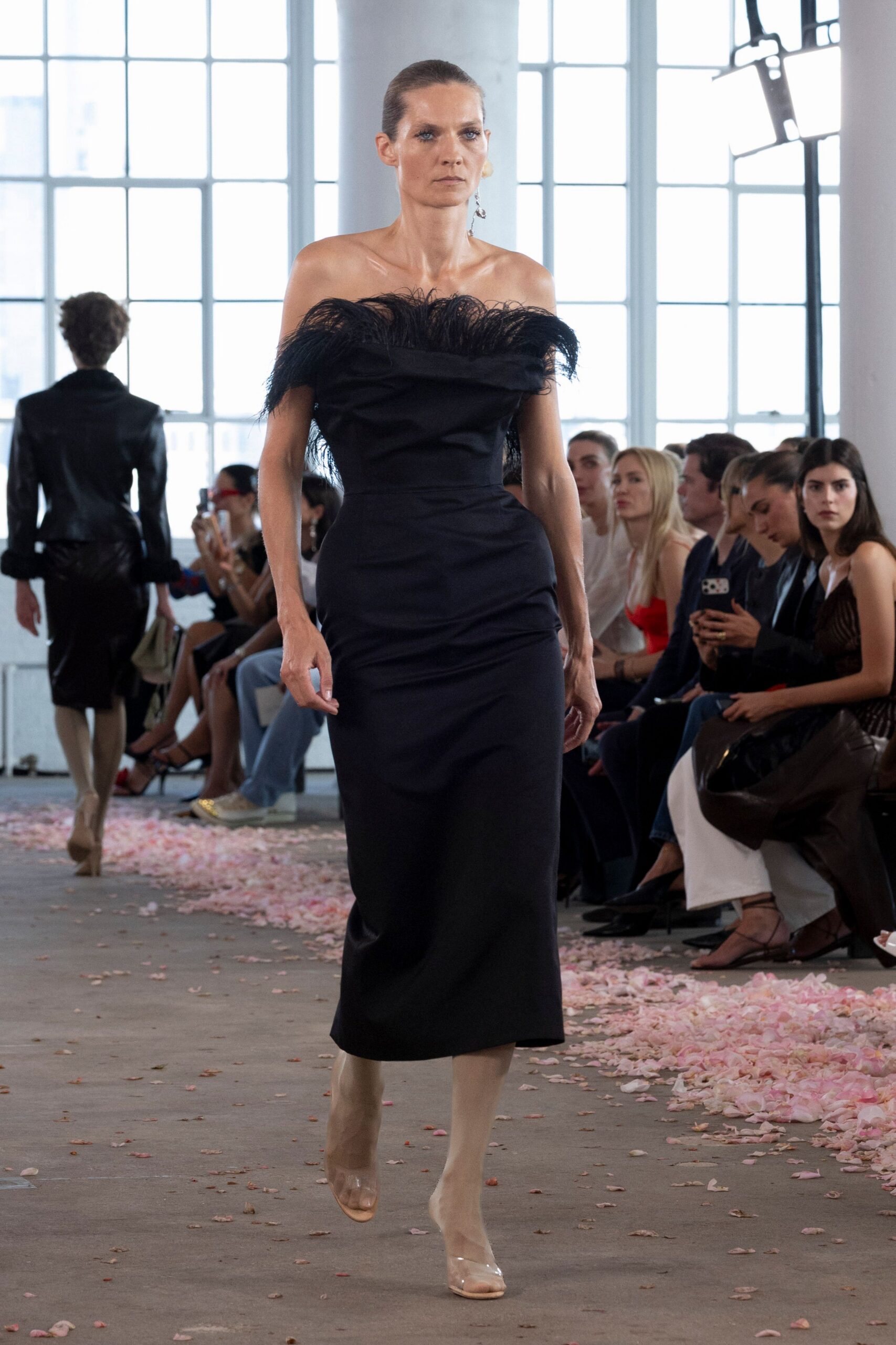 Black satin column dress, off-the-shoulder neckline ringed with airy black feathers. Clear PVC peep-toe heels with a nude insole. Single dangling crystal earring. Walking the length of a loft still littered with crushed rose petals.