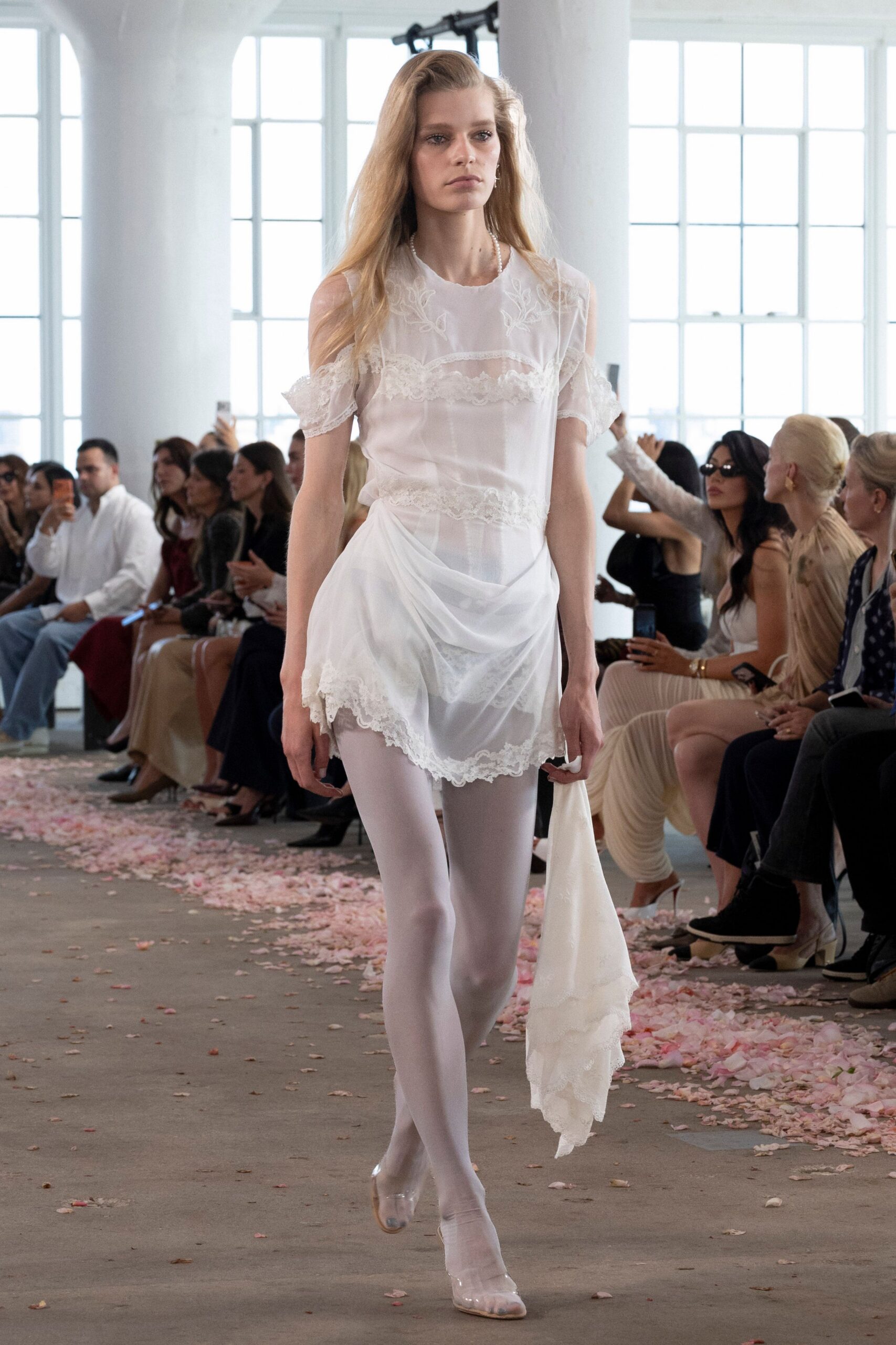 Sheer white slip dress with lace bands and dropped off-shoulder sleeves. Opaque white tights under the gauzy draped mini hem. Clear vinyl pumps with a milky pointed toe. Long ivory chiffon scarf, lace edging brushing the floor. Crossing a conservatory aisle after the flower girl spilled both baskets.