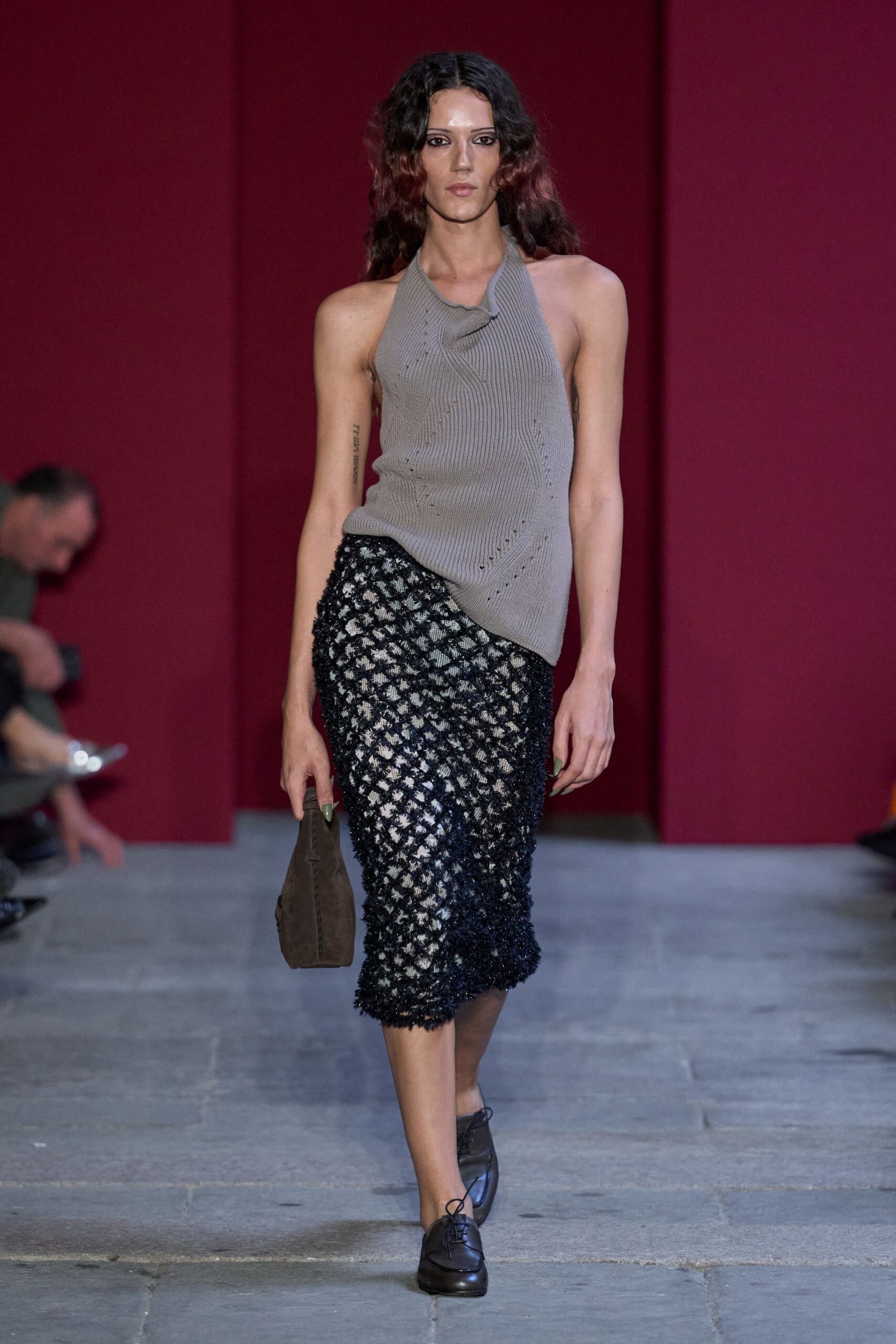 Taupe rib-knit halter, twisted cowl neckline and tiny laddered pointelle lines. Black openwork pencil skirt with shaggy fringe catching over a pale lining. Brown suede pouch, folded flat in the hand. Dark leather lace-up flats with a squared apron toe. Walking back from a matinee with rain still drying on the pavement.
