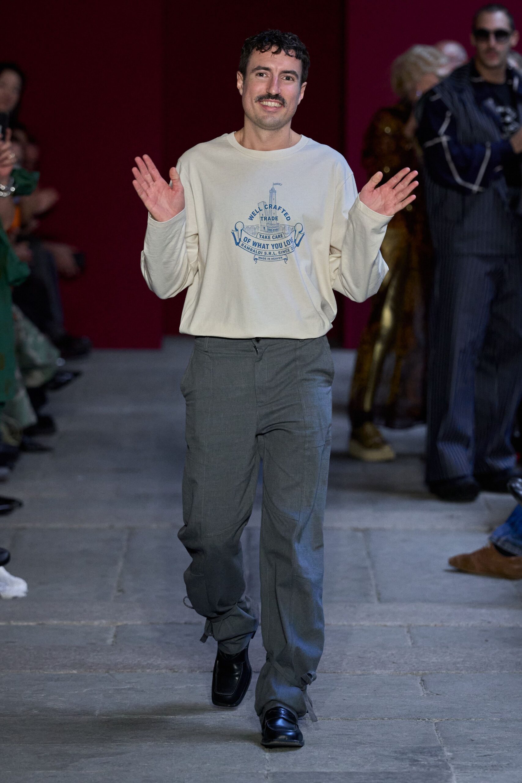 Cream cotton jersey tee with a faded blue chest graphic. Grey straight-leg trousers with flap cargo pockets and loose ankle ties. Black square-toe leather loafers. Walking across cold flagstones after everyone else has gone home.