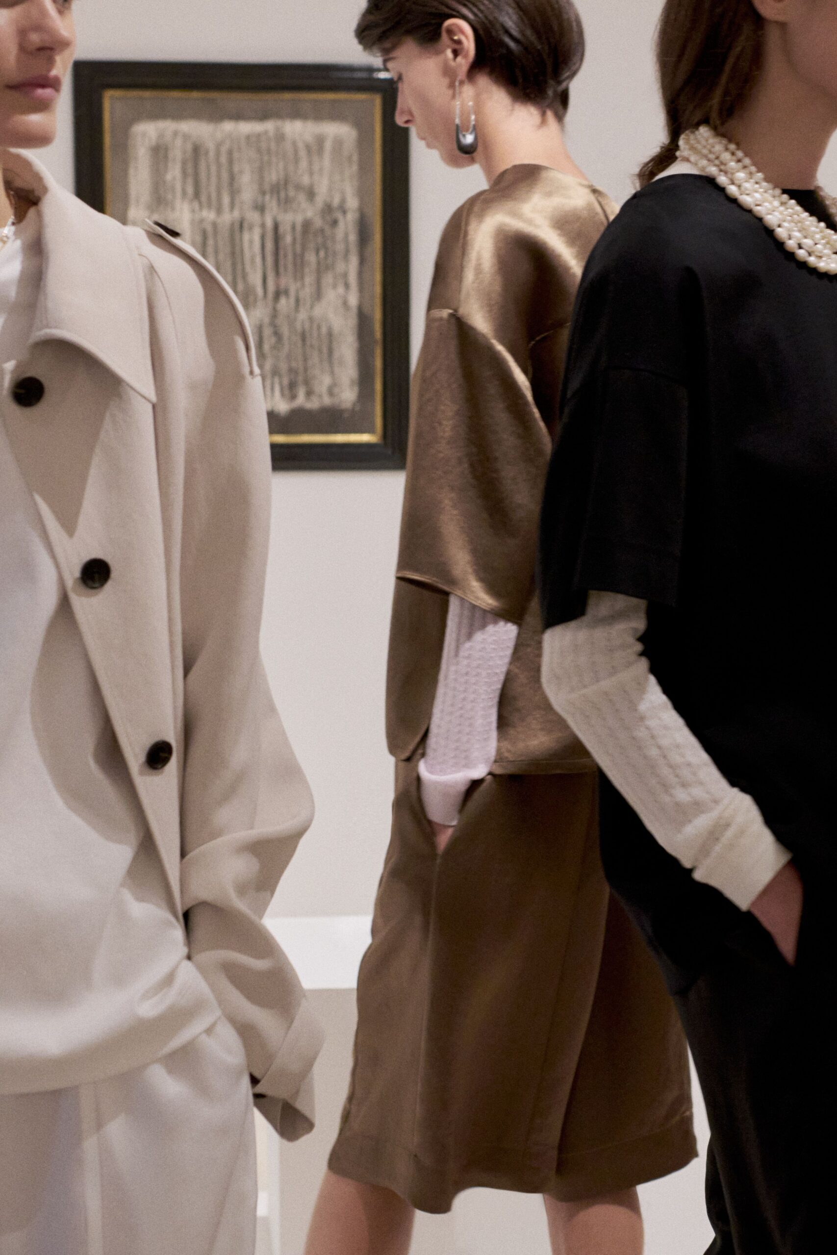 Bronze satin top with a hard sheen and cropped split sleeves. White honeycomb knit layer, cuff peeking below the elbow. Matching bronze satin shorts cut full and almost skirt-wide. Oversized dipped-drop hoops. Walking through a quiet gallery before the speeches and warm white wine.