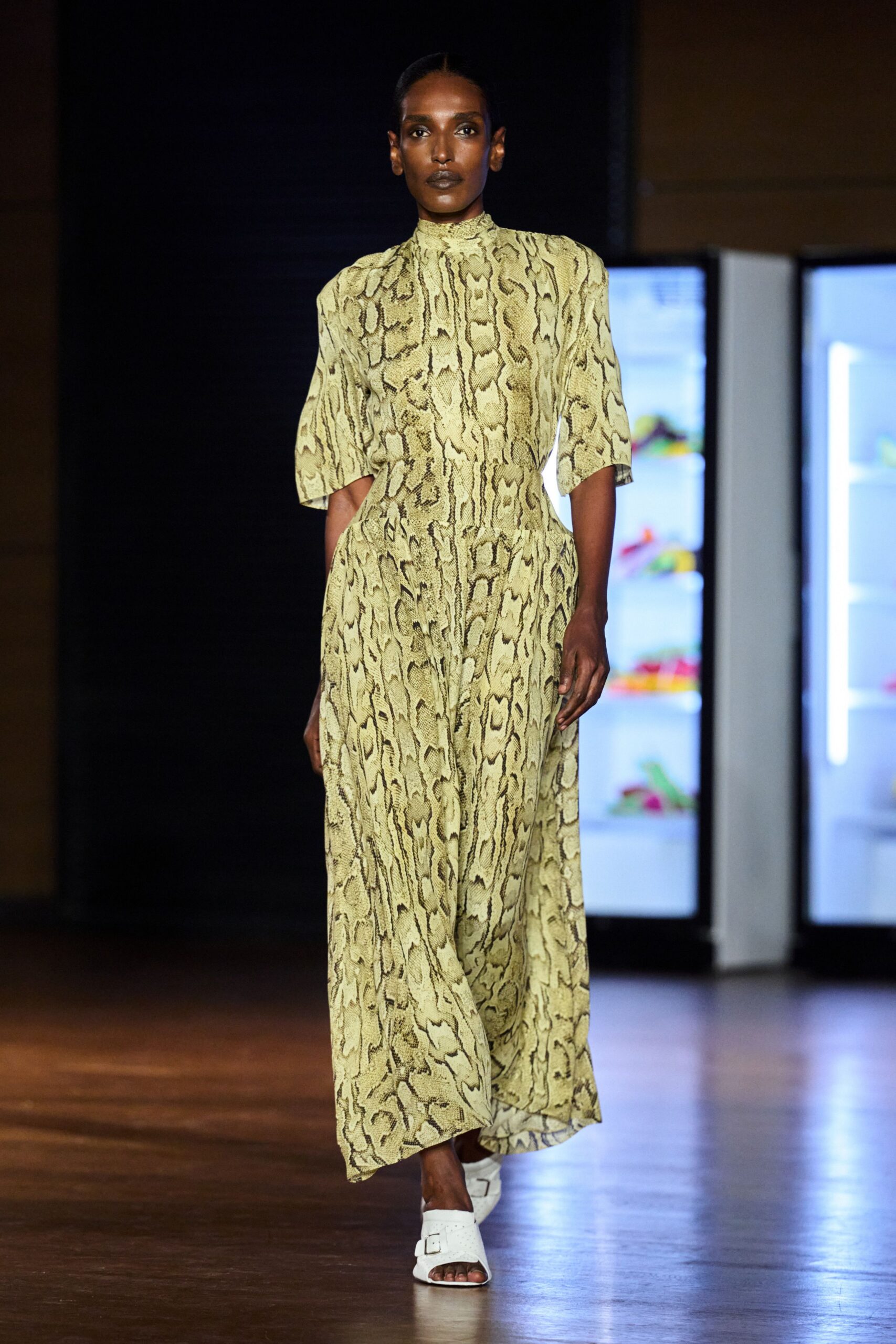 Pale python-print dress with a ruched stand collar and dropped waist. White leather slide sandals with a single square buckle. Walking through a design museum after the school groups have gone.