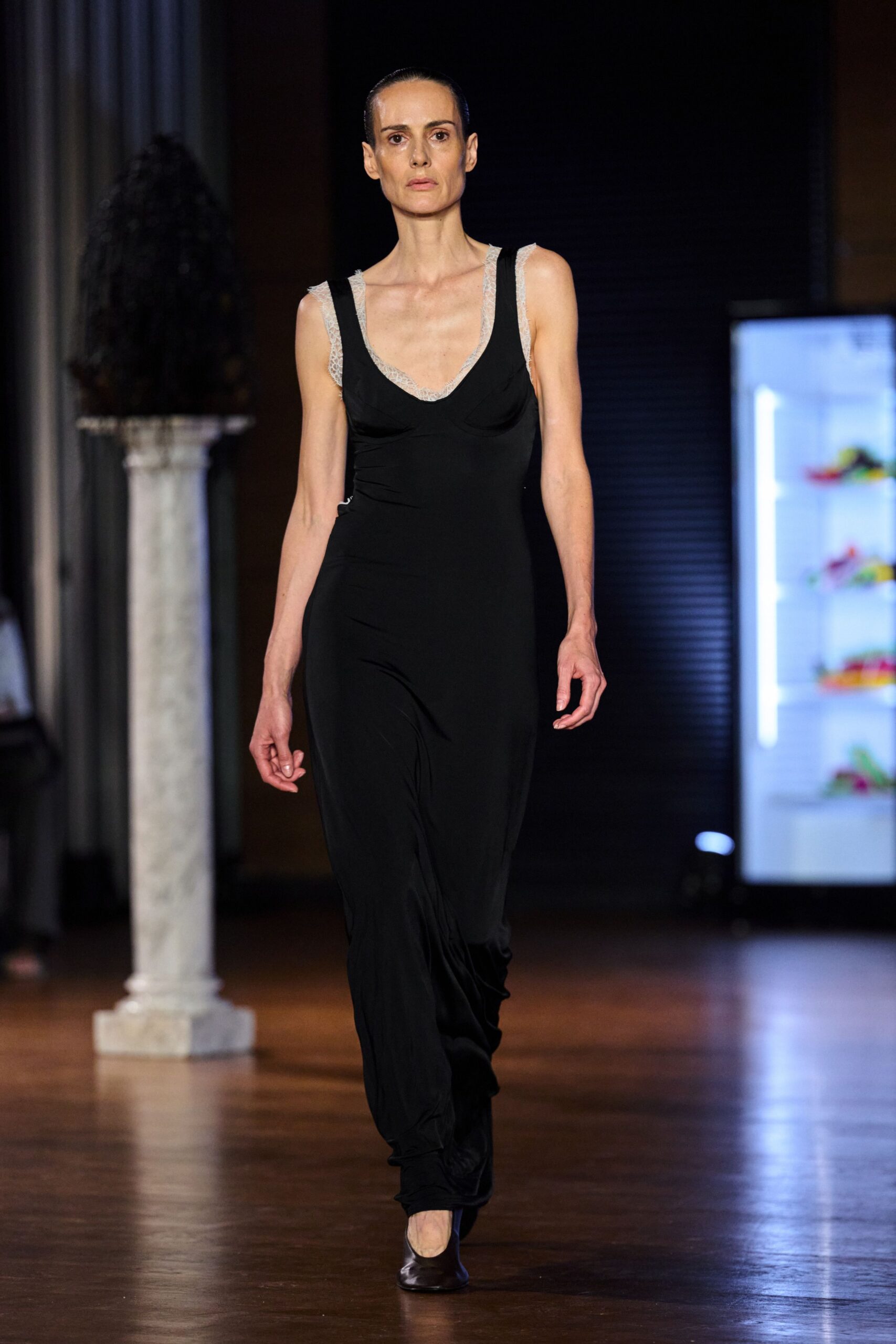 Black jersey slipdress with a low scoop, seamed cups and pooling hem. Pale lace camisole edging the neckline and straps with a soft scallop. Dark square-toe flats in brushed leather. Whatever you wear downstairs at dawn in a hotel gone quiet after the wedding.
