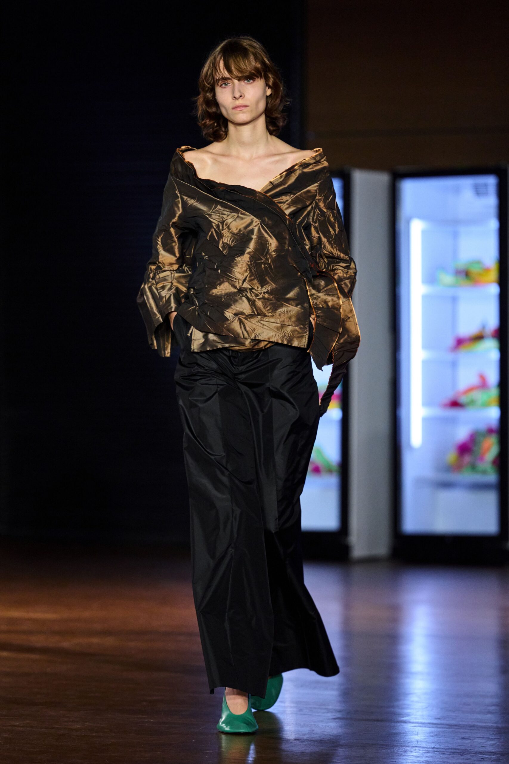 Bronze shot taffeta wrap top, crushed and slipping off both shoulders. Black nylon wide-leg trousers with a soft break over the foot. Glossy jade square-toe flats. Walking the office corridor after midnight, vending machines buzzing blue.