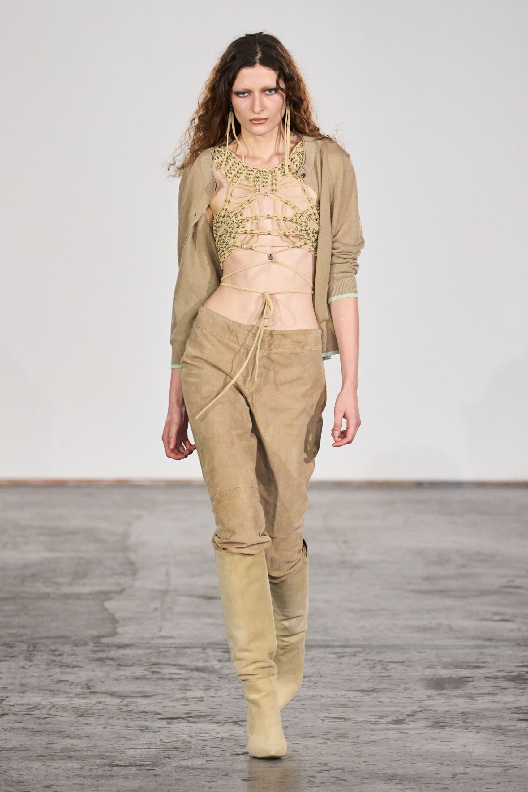 Taupe fine-knit cardigan worn open, cuffs tipped in pale mint. Beige macrame cropped top, webbed openwork tied round the bare waist. Low-slung sand suede trousers, one long drawcord hanging past the fly. Pale suede knee boots. For crossing a dry riverbed after the sun has gone down.
