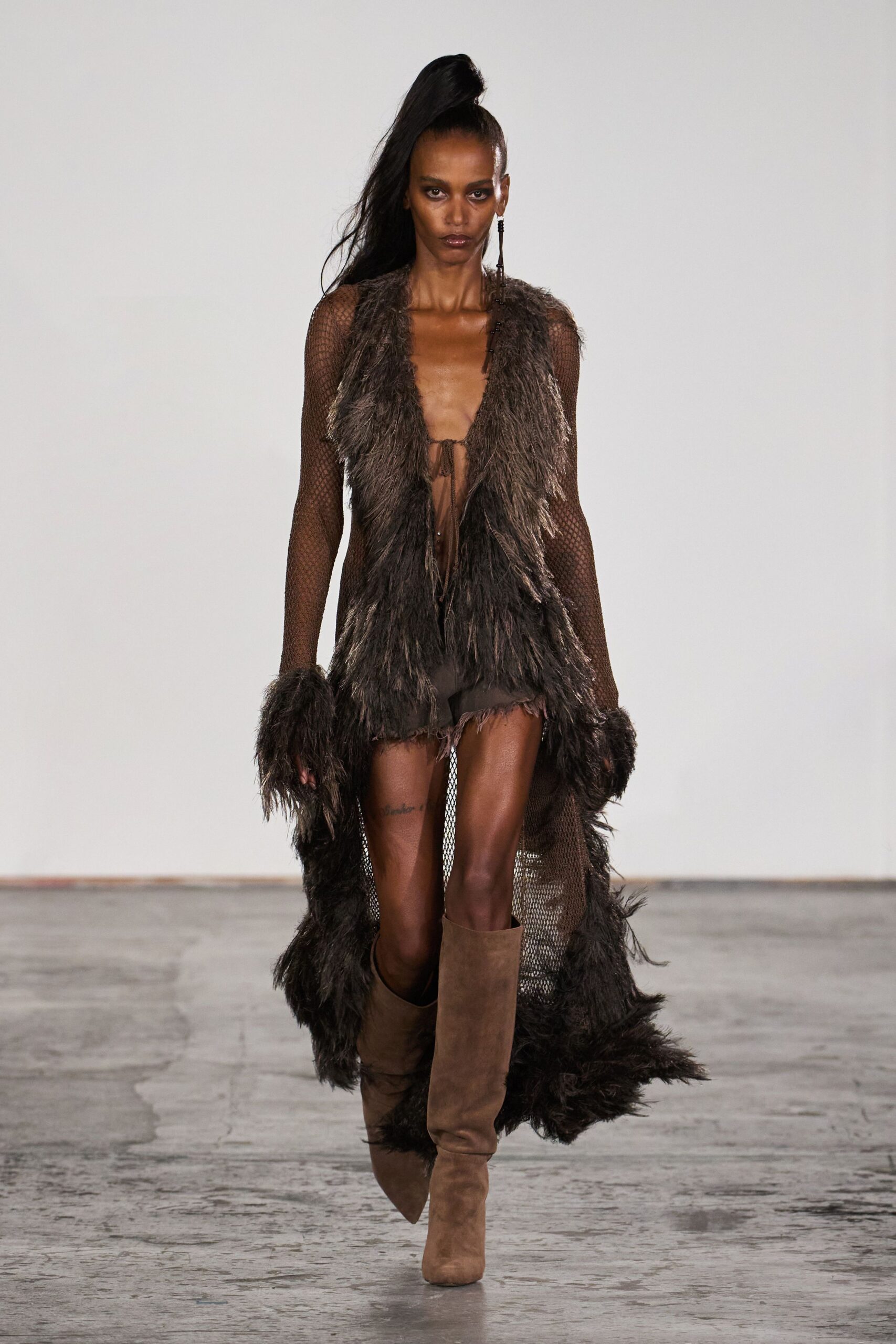 Single beaded tassel earring brushing the collarbone. Brown fishnet dress veiled in shaggy faux fur, tied by two chest cords. Taupe suede knee boots with slouched shafts and pointed toes. For crossing a motel parking lot before dawn with your shoes in hand.