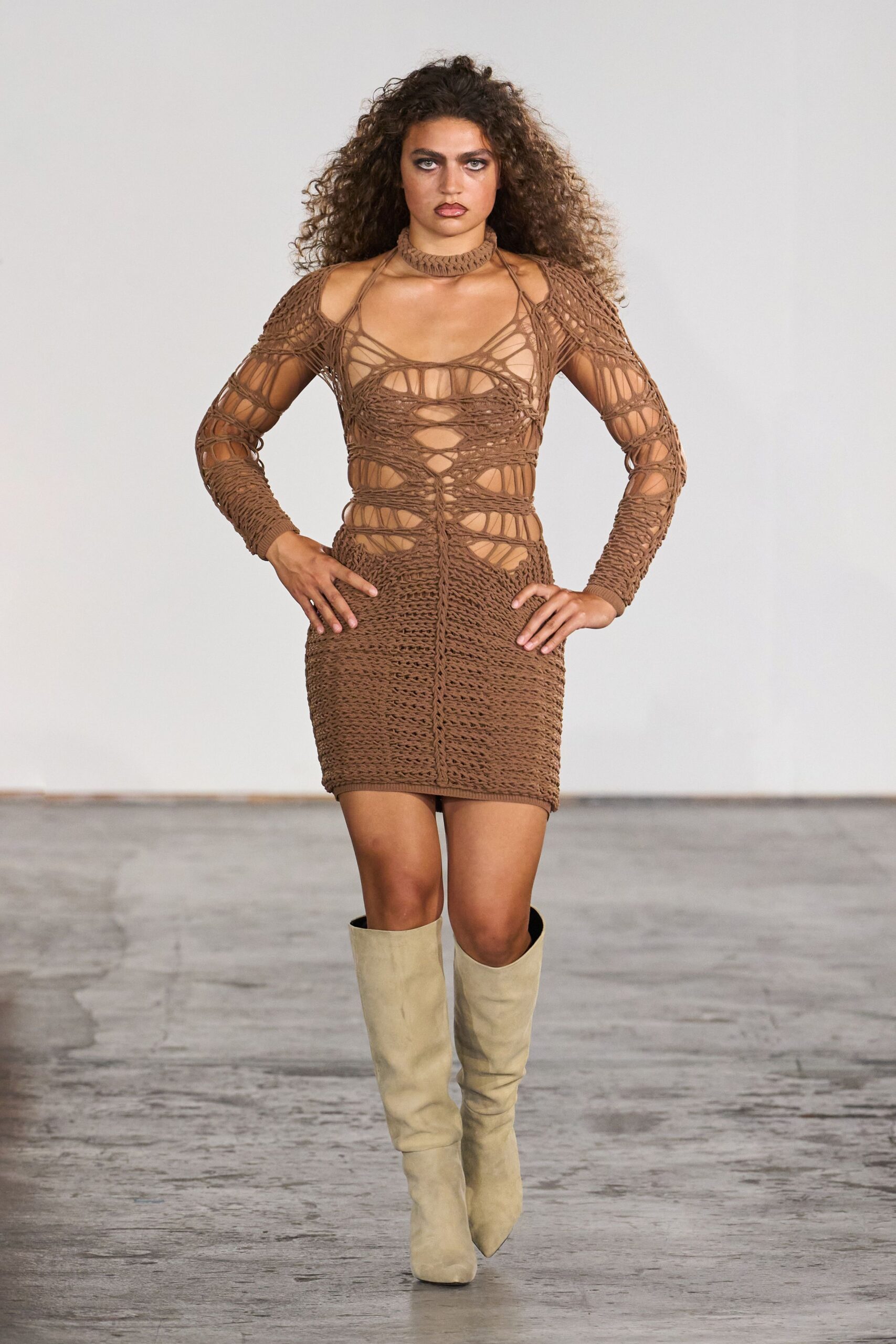 Openwork knit choker in cocoa yarn, snug at the throat. Cocoa string-knit mini dress, spiderweb cutouts exposing shoulders, ribs and sternum. Pale suede knee boots with softly slouched shafts and pointed toes. Walking out of a desert rental after the pool has gone cold.