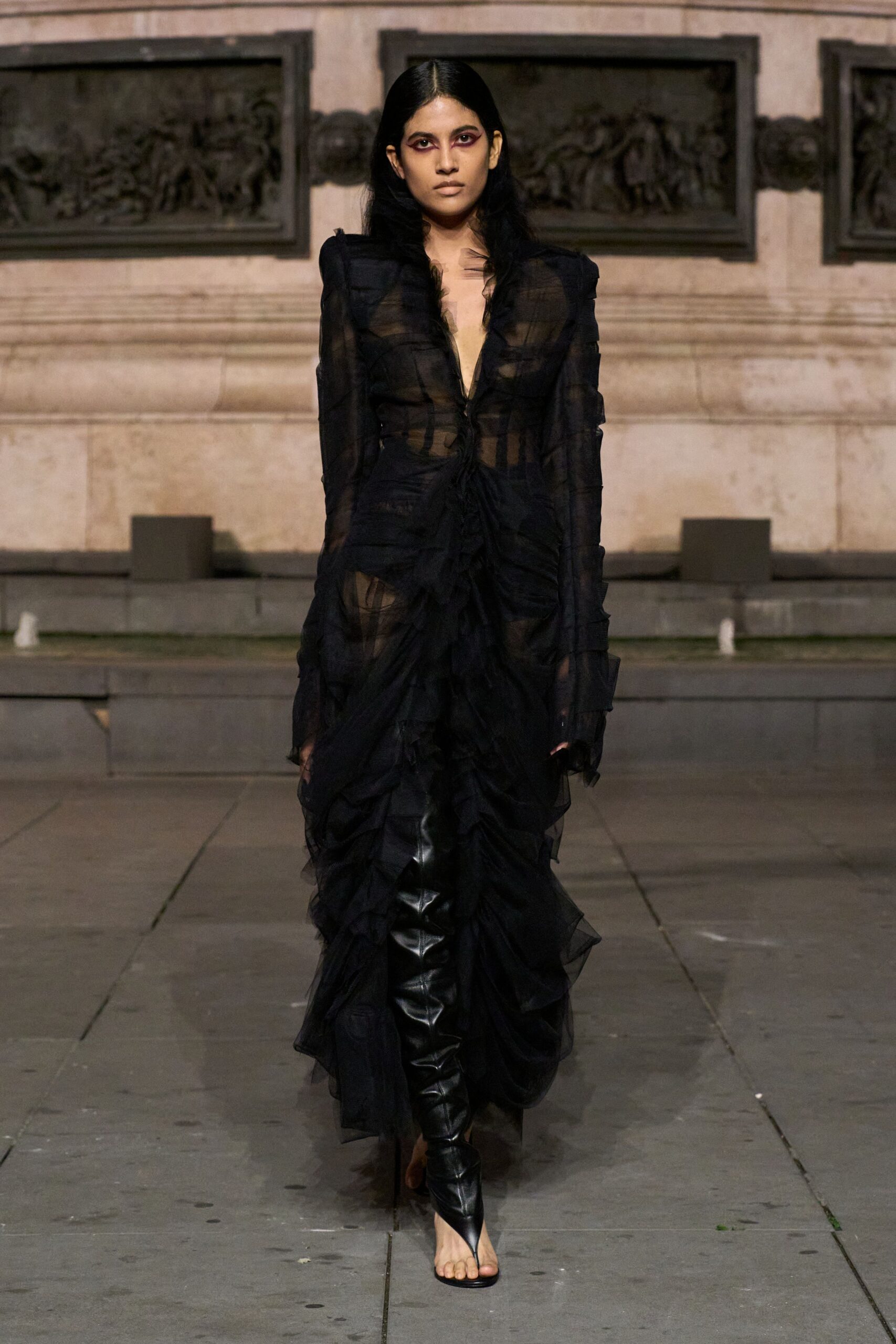 Sheer black organza dress, plunged to the waist and ruched into tiered ruffles. Glossy black thigh-high boots with split-toe thong sandals peeking bare toes. Crossing a stone courtyard after midnight mass, eyeliner not yet smudged.