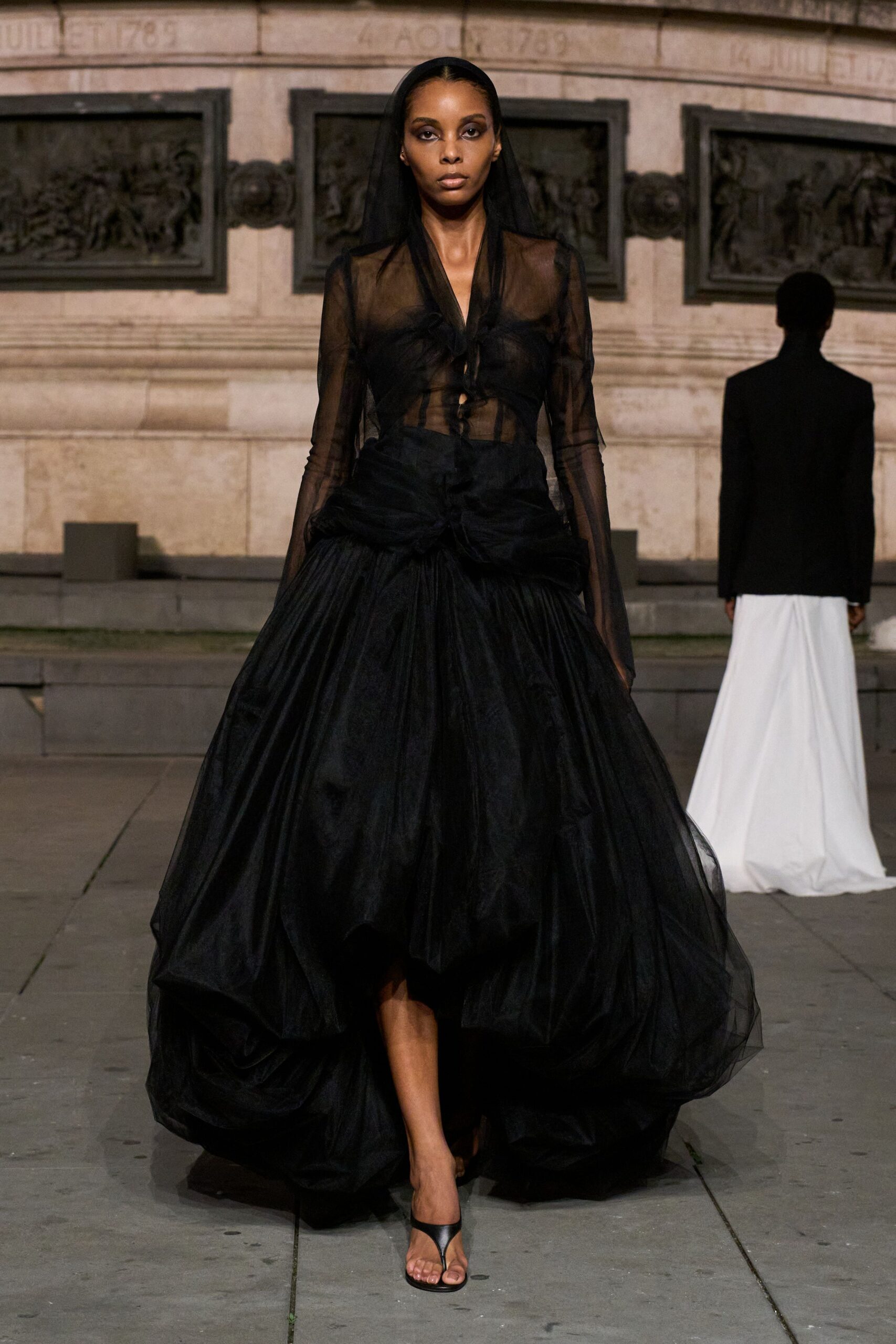 Sheer black organza blouse, self-ties knotted loosely down the open front. Black taffeta skirt ballooned into a vast drop-waist cocoon. Black thong heels. Crossing a stone square after midnight with opera makeup still on.