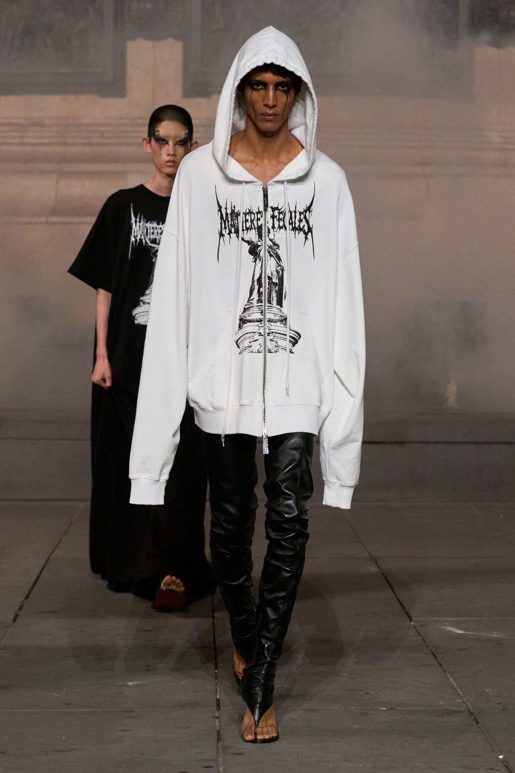 Oversized white jersey zip hoodie, black spiked lettering over a statue print. Black leather leggings, wrinkled tight through the shin. Barely there thong-strap heels. Crossing a stone square after midnight while they hose it down.