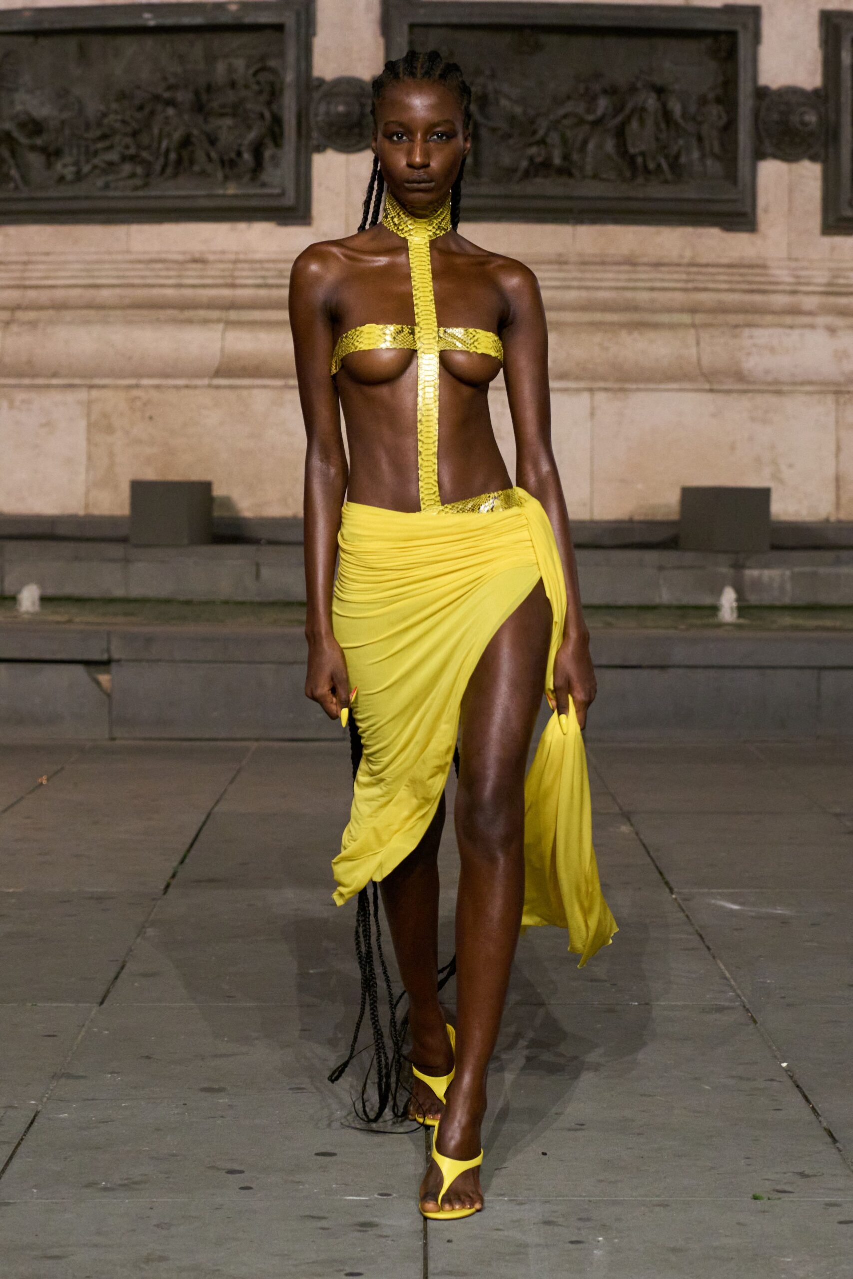 Acid-yellow python strips form a collar, center spine and bandeau. Ruched jersey sarong skirt, hitched high with a trailing side panel. Matching thong heels with a slim stiletto. Heat still rising off the plaza stones after the fountains shut off.
