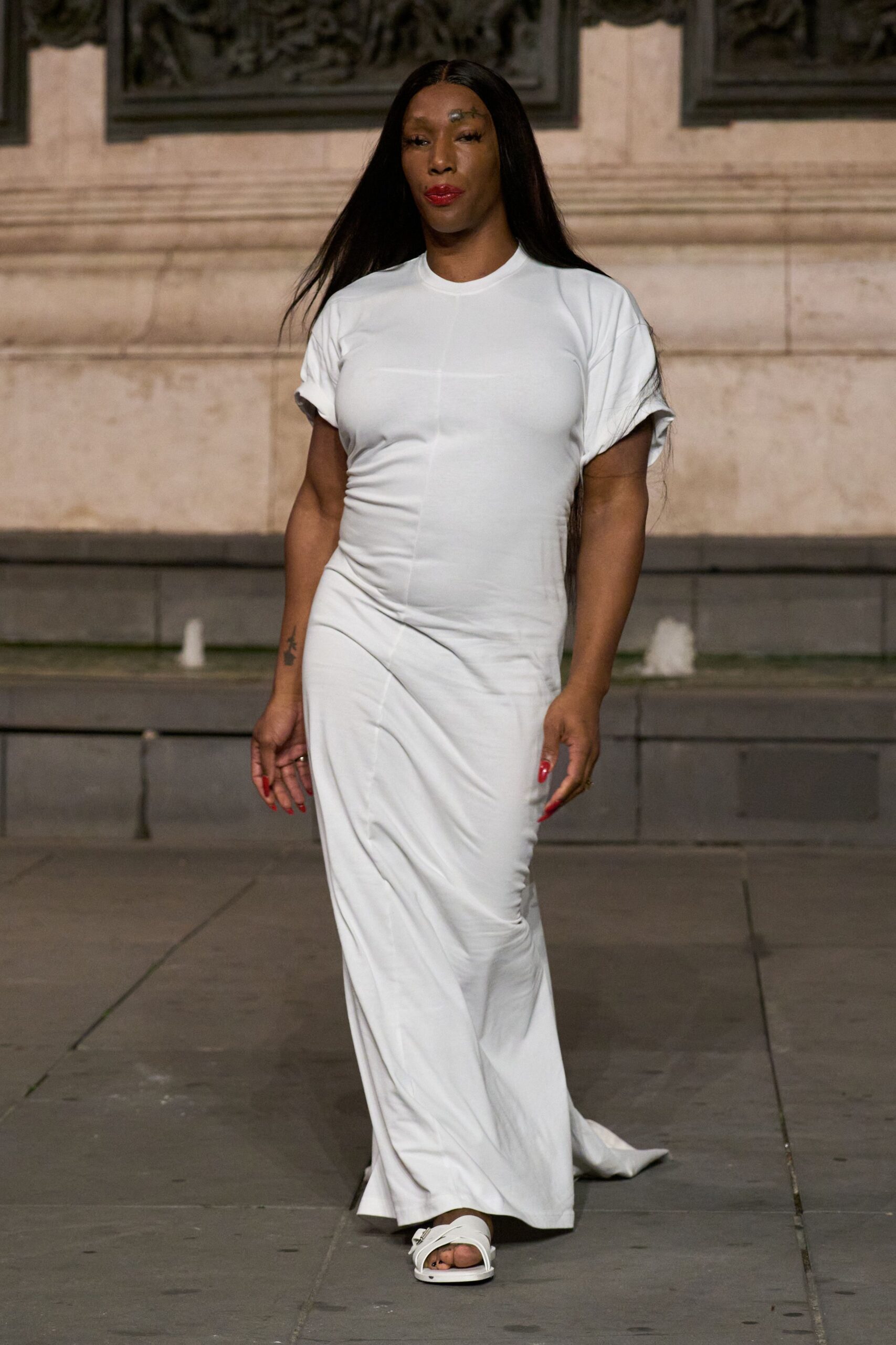 White jersey column dress cut like a tee, rolled cuffs and center seam. White leather slides with broad crisscross straps and squared soles. Crossing a stone courtyard just after the fountain shuts off.