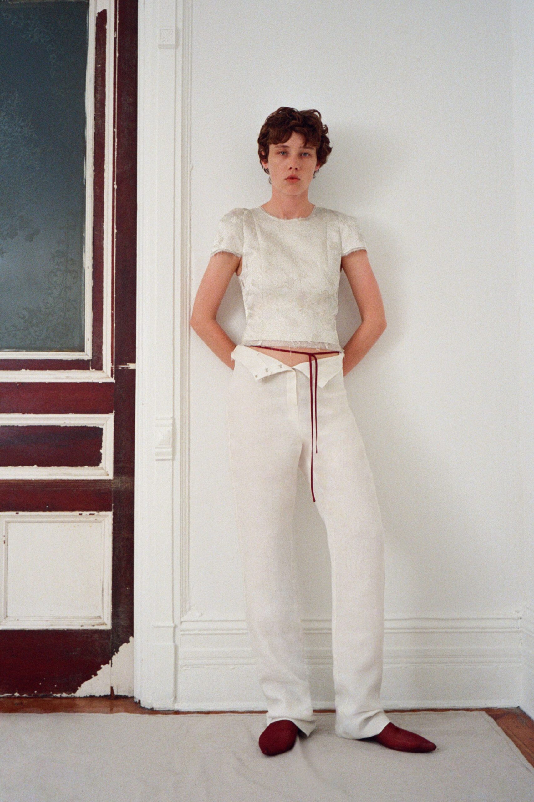 Ivory brocade top with puffed cap sleeves and a raw lower edge. Wide ivory trousers, waistband folded down and cinched with burgundy cord. Burgundy flats with a soft slipper shape. Sunday in a drafty apartment before the guests arrive for lunch.