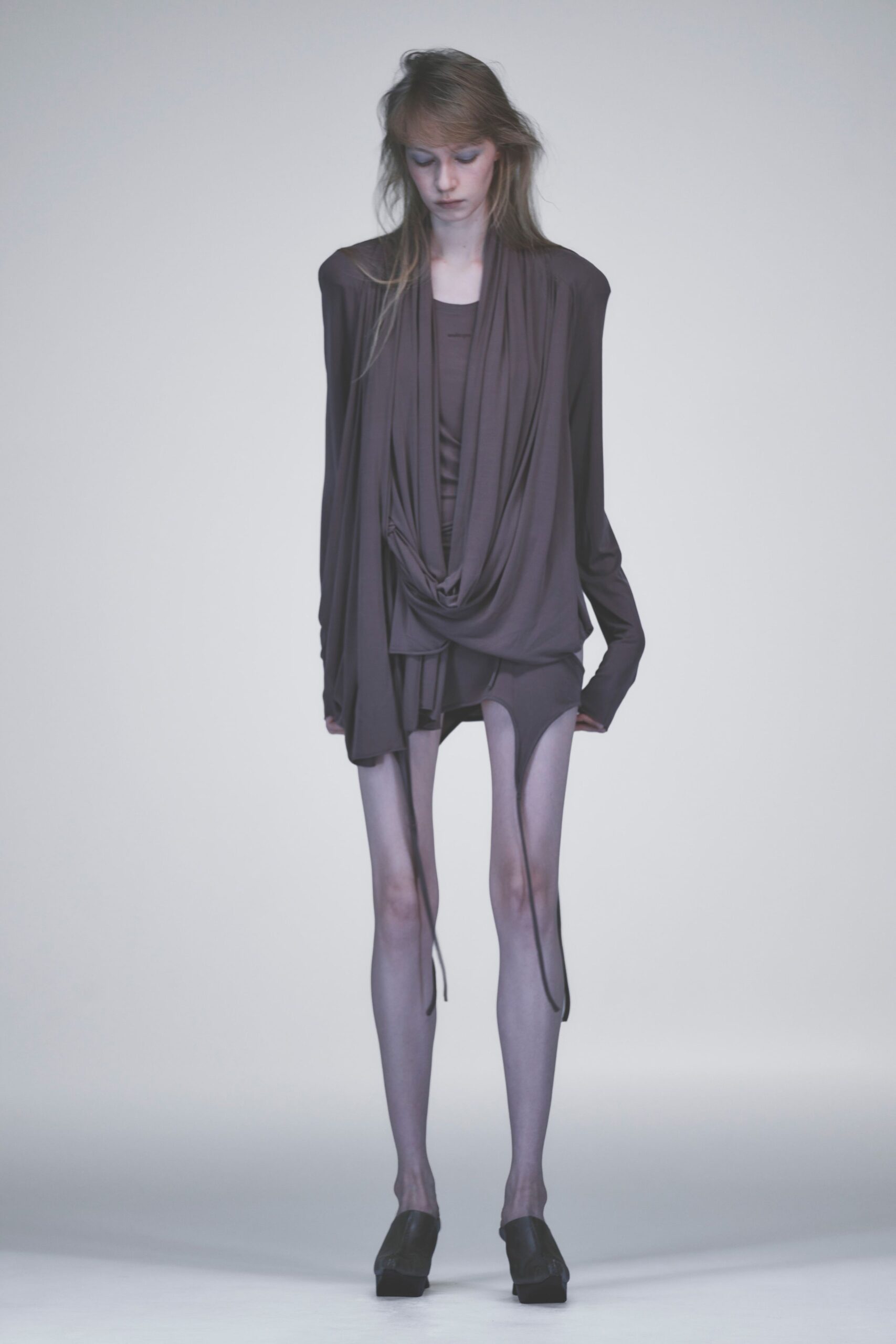 Smoke-plum jersey top with a cowl loop hanging almost to the thighs. Matching bodysuit cut high at the hip, a small horizontal bar at the chest. Ash sheer tights with dark seams dropping from the briefs. Black leather platform mules. Whatever you wear home after sleeping through someone else's afternoon.