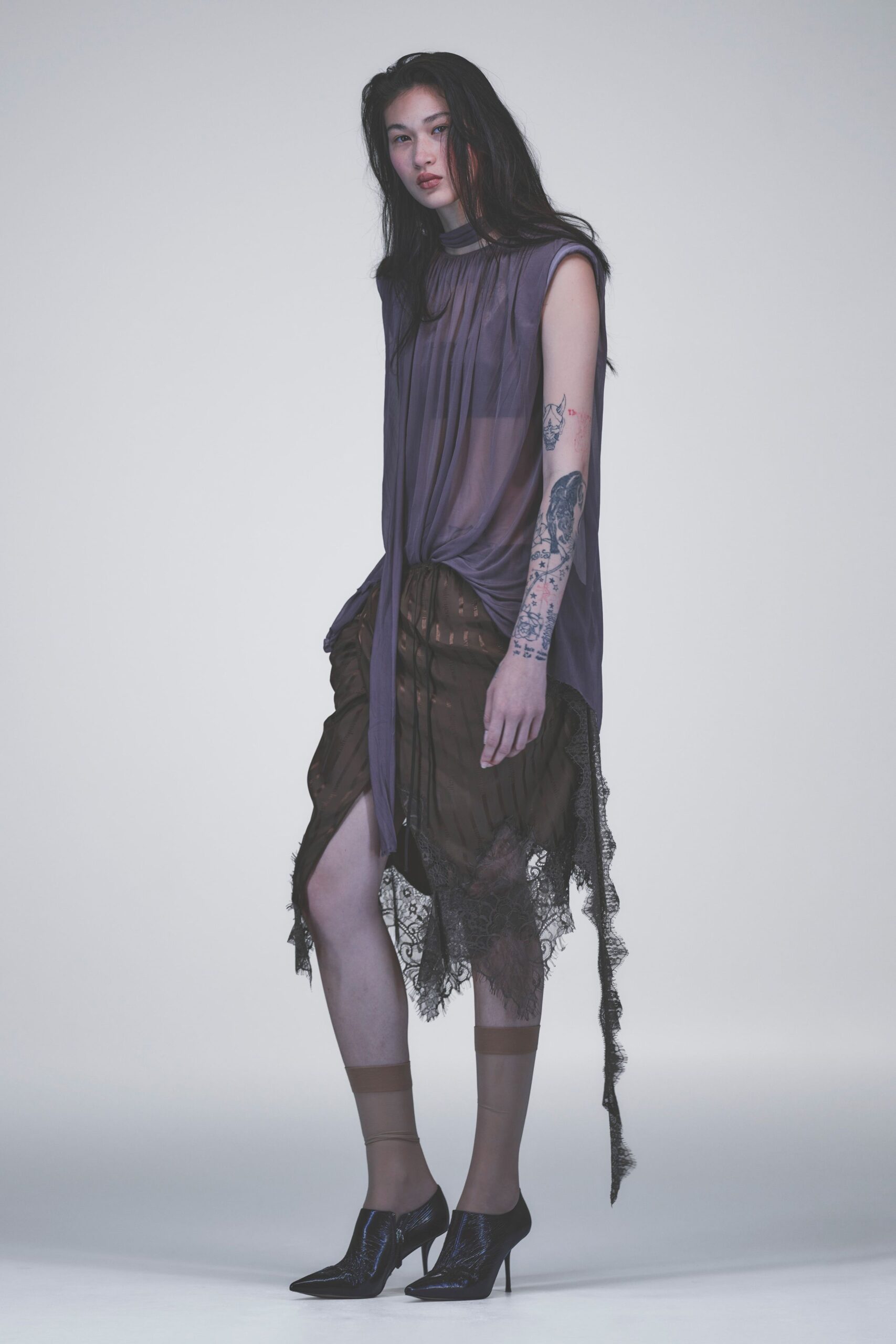 Smoky mauve chiffon top, pleated from a narrow mock neck. Brown sheer skirt with laddered stripes and black lace hanging loose. Sheer nude ankle socks with a denser cuff band. Black patent pumps cut high and pinched to a pointed toe. Whatever you wear home after dawn with your makeup still mostly intact.