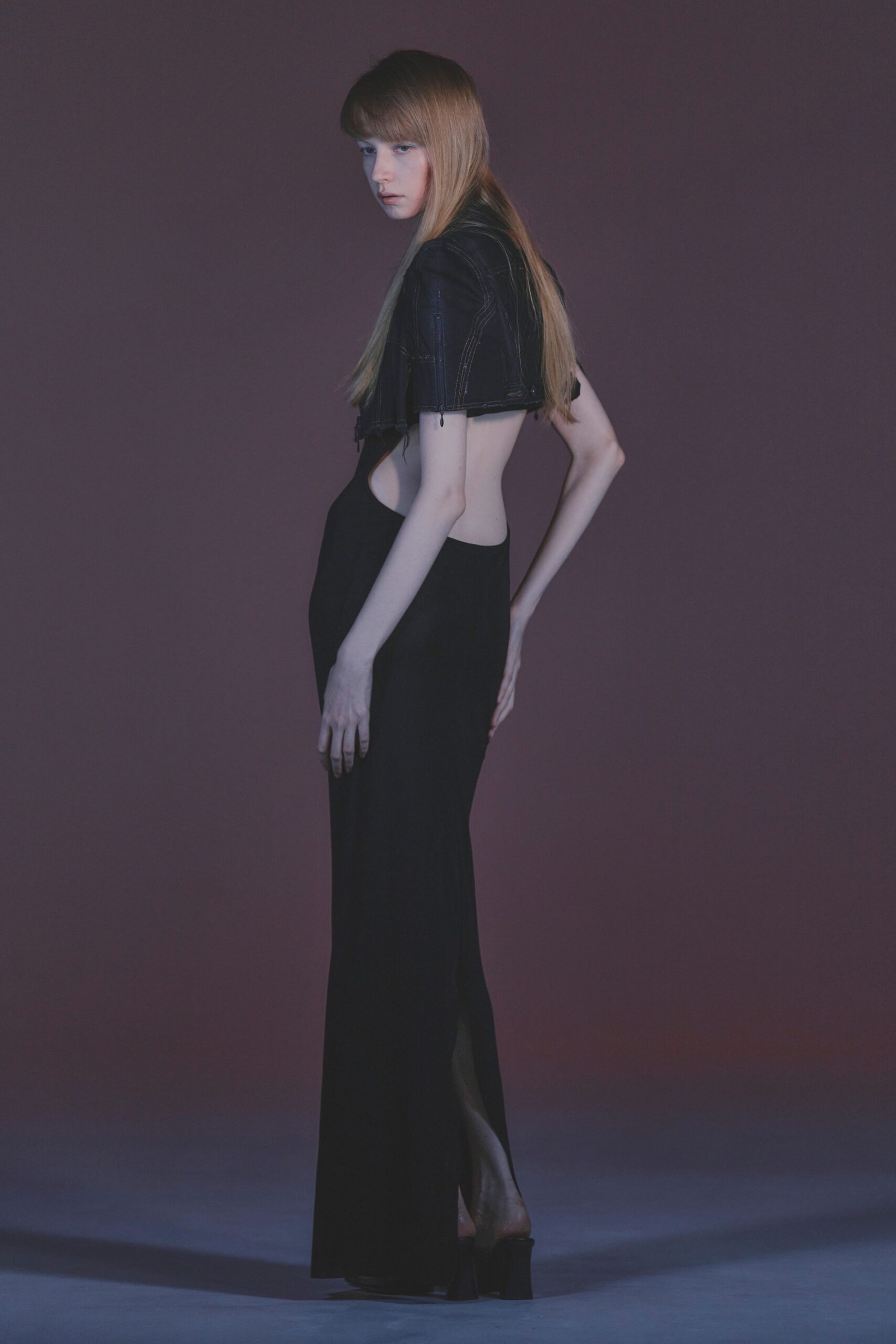 Cropped black denim bolero with stark white topstitching and dangling zip pulls. Black column gown cut away to the ribs, falling to a back slit. Black platform mules. Whatever you wear home after the hotel bar piano has stopped.