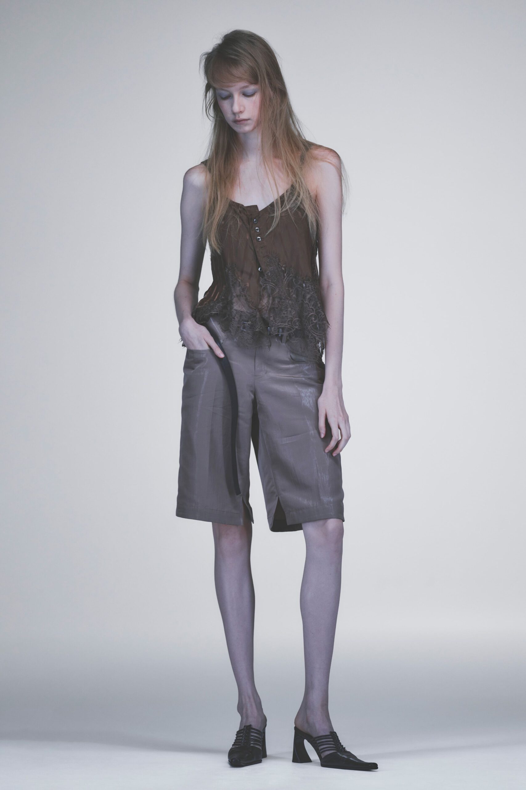 Chocolate camisole with a jagged lace hem and four tiny buttons. Taupe knee-length shorts in a faintly glazed cloth, front crease held sharp. Black caged mules with a squared vamp and flared heel. The hour before rain hits, crossing an office plaza barefoot in your head.
