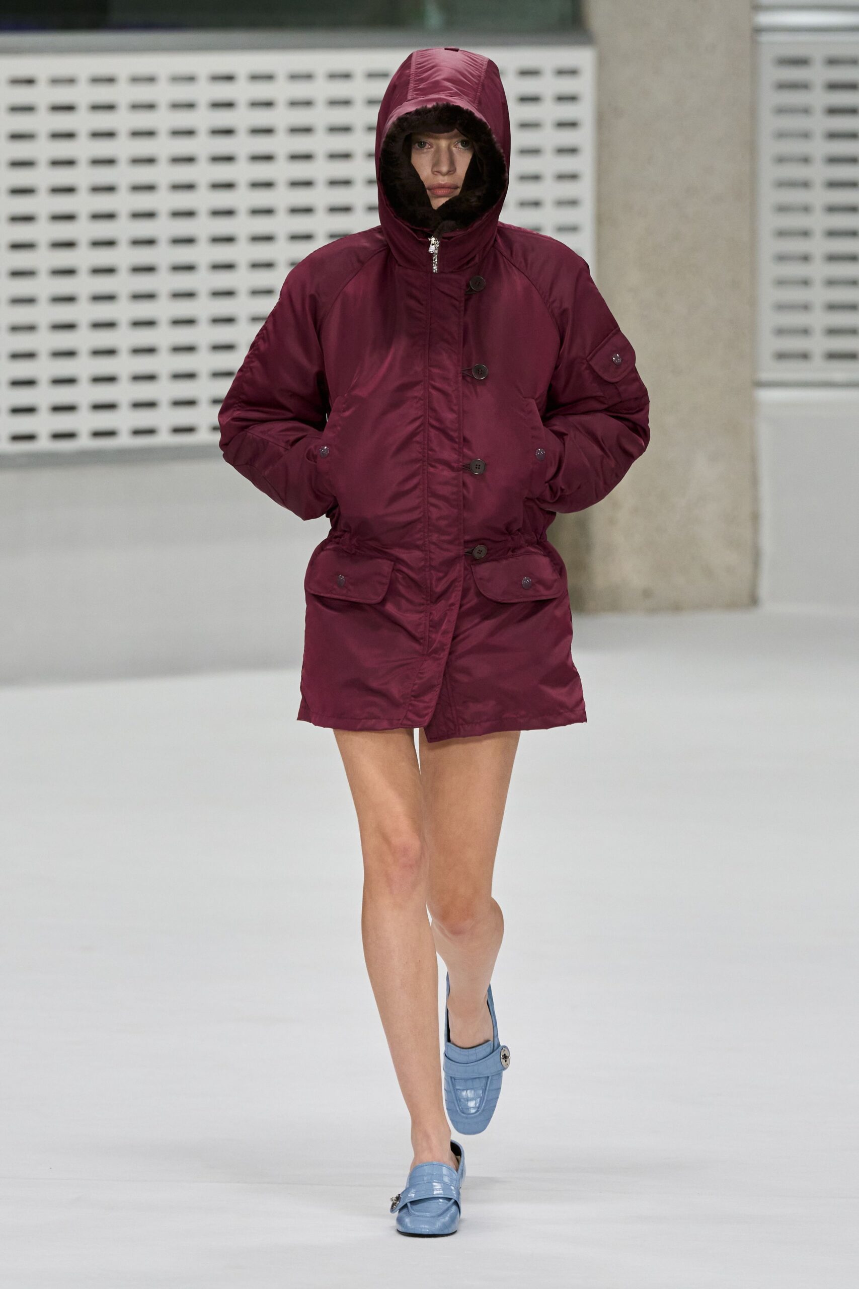 Burgundy nylon parka, hood ringed in dark pile with oversized flap pockets. Powder-blue croc-embossed leather mules, one strap hanging behind the heel. For the first cigarette outside a ski lodge after midnight.