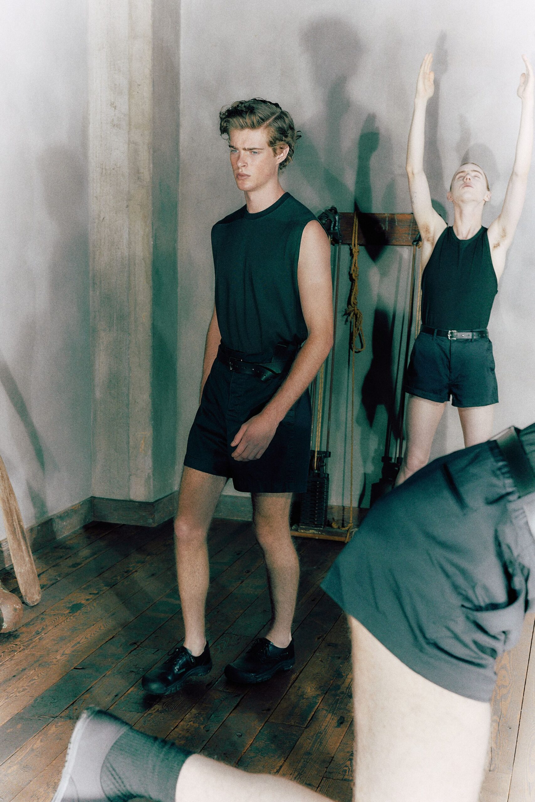 Black sleeveless tank with a narrow ribbed neck binding. Black leather belt, buckle sitting slightly off center. High-waisted black shorts in crisp cotton twill. Black leather derbies with thick rounded soles. For crossing a gym floor after everyone else has gone home.