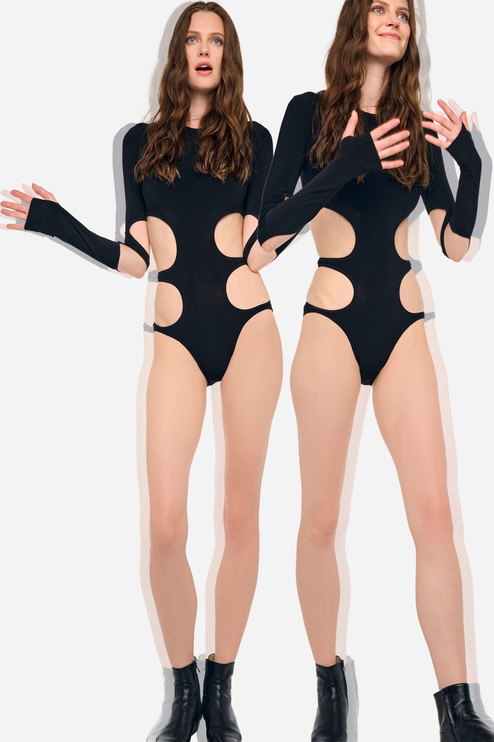 Black stretch bodysuit with oversized oval side cutouts and thumbhole sleeves. Black leather ankle boots with a slim shaft and plain toe. Under rehearsal fluorescents after someone suggests cutting the song shorter.