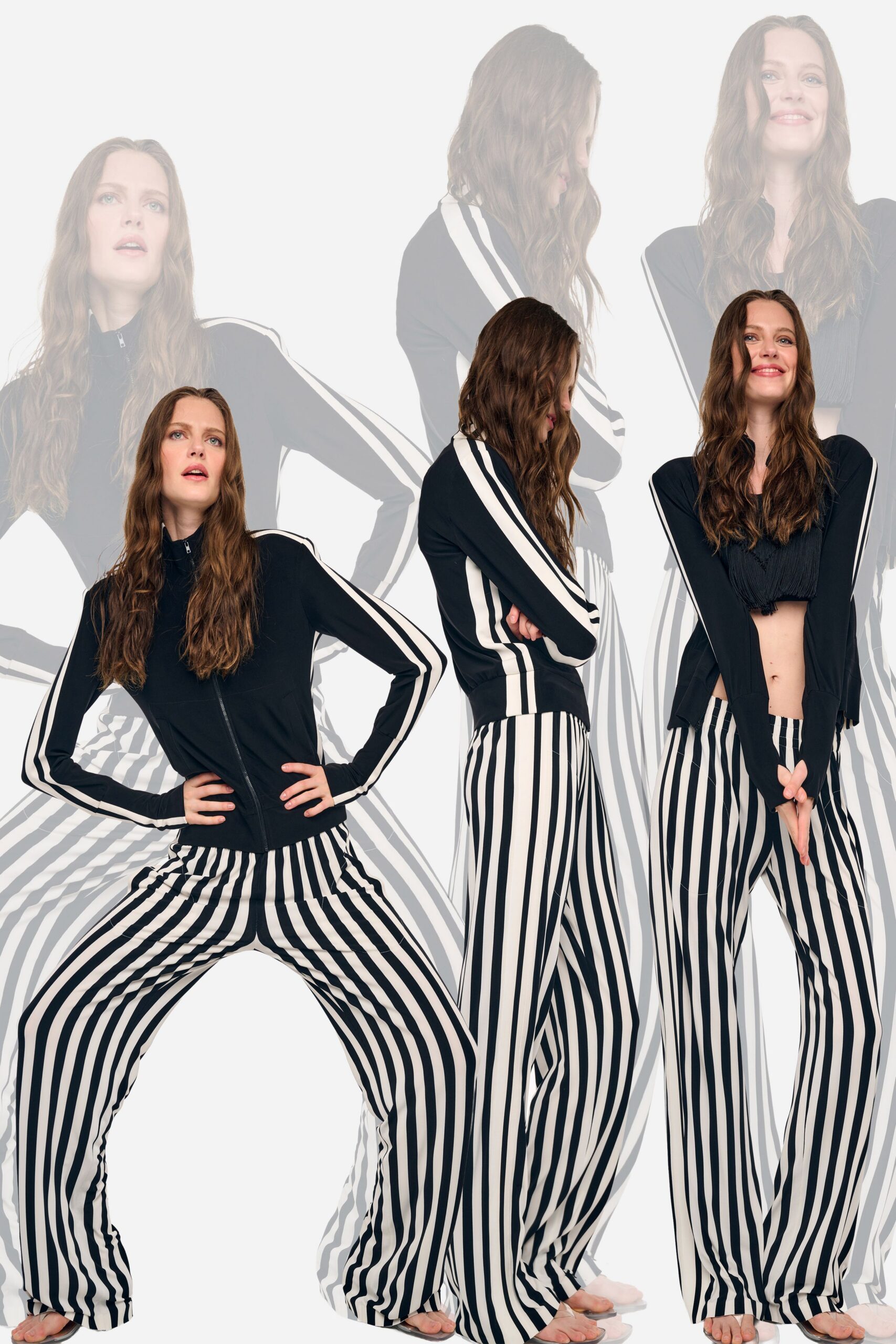 Black knit track jacket with twin ivory sleeve stripes and a high zip neck. Black cropped top with dense tassel fringe brushing the ribs. Fluid wide-leg trousers in stark black-and-white vertical stripes. Walking barefoot across a rental house kitchen the morning after the party.