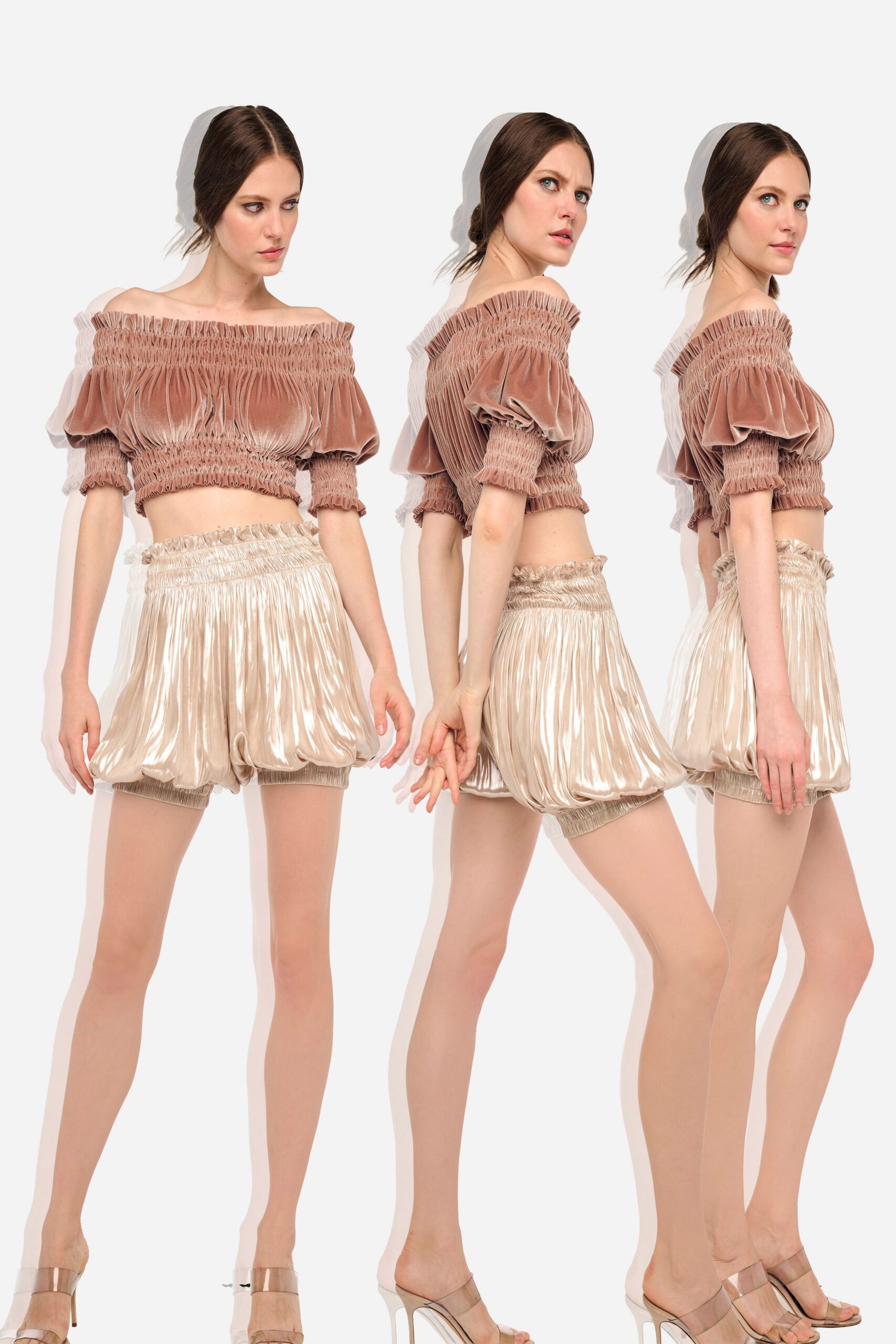 Dusty rose velvet crop top with smocked bands and puff sleeves. Champagne lamé bubble shorts, paperbag waist ruffling above the hip. Clear strap stiletto mules. Rooftop baby shower just before the sun drops behind the towers.