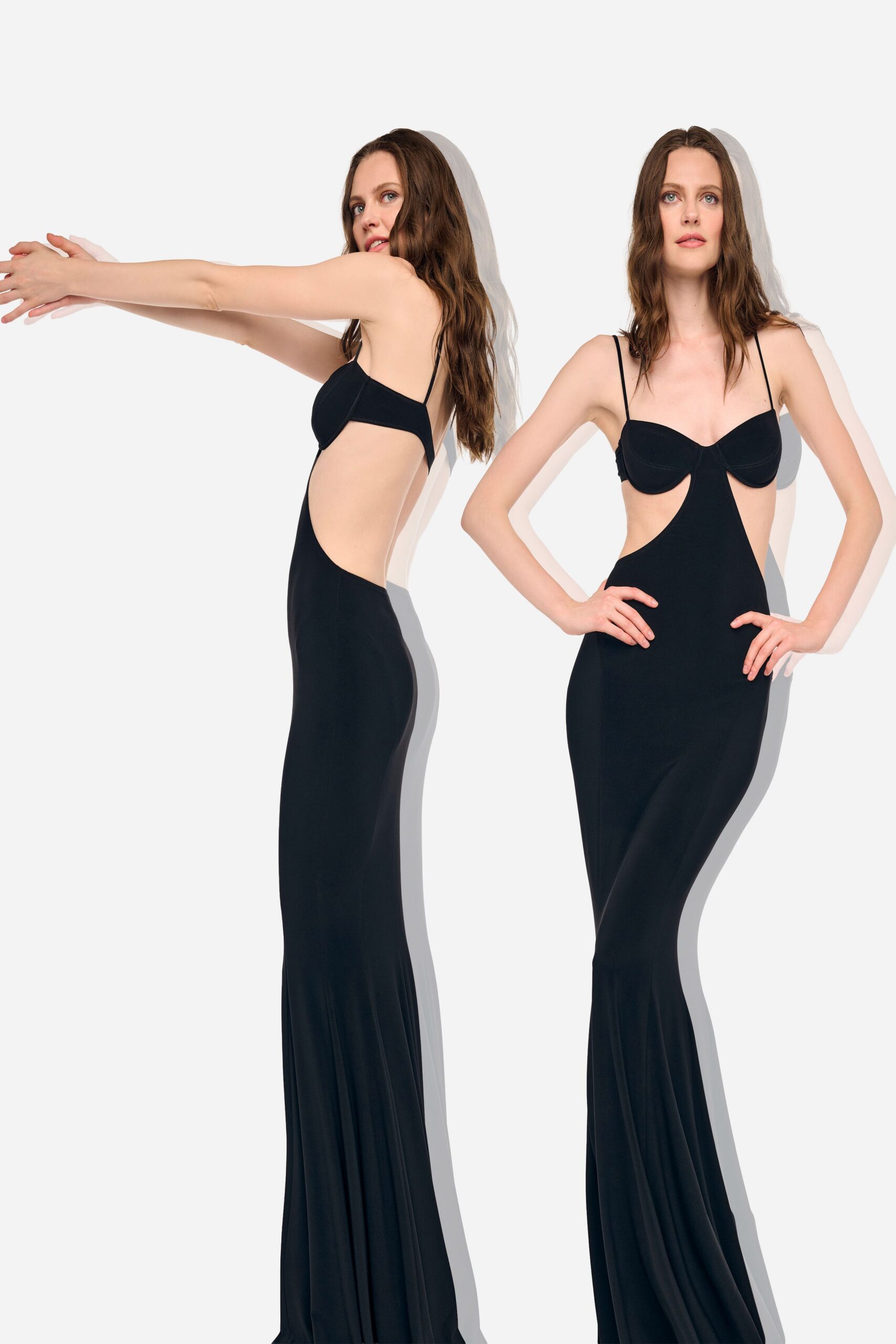 Black jersey column gown with underwired bra cups and deep side cutouts. Fine spaghetti straps tracing bare shoulders. Floor-length skirt loosening into a slight fishtail ripple. For the hotel corridor after midnight, ice bucket still sweating in your hand.