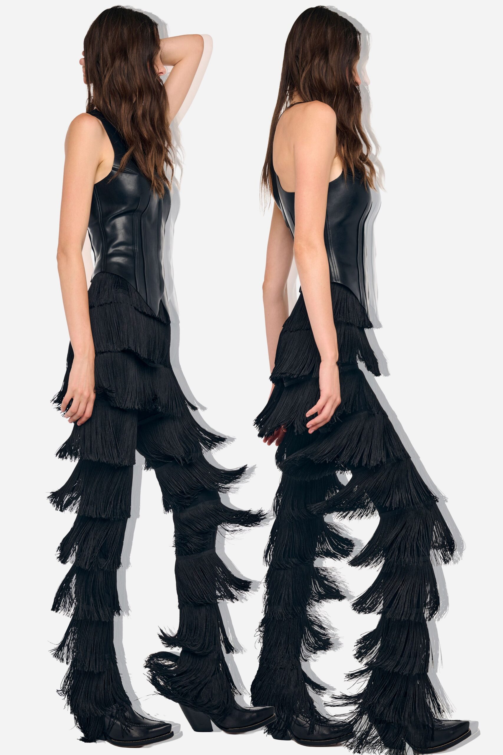 Black leather tank top, princess seams carving to a dipped point hem. Black trousers buried under tiered fringe, one loose swath kicking off the calf. Pointed black boots with low angled heels peeking through the strands. Crossing a fairground after dark while the generators still hum.