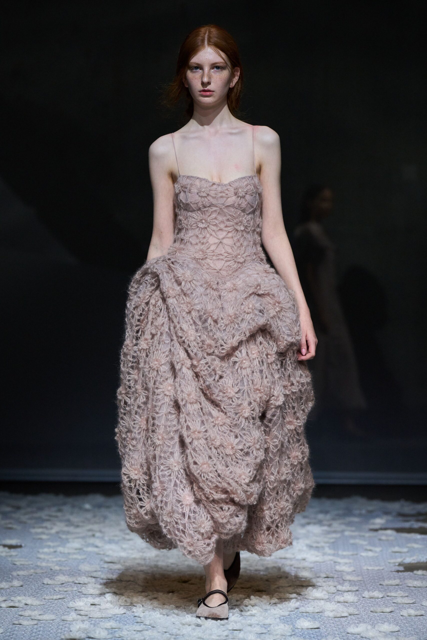 Blush spaghetti-strap dress in looped floral lace, skirt ballooned into gathered swags. Pale pointed flats with a narrow black instep strap. Crossing a wedding lawn after the chairs have been folded away.