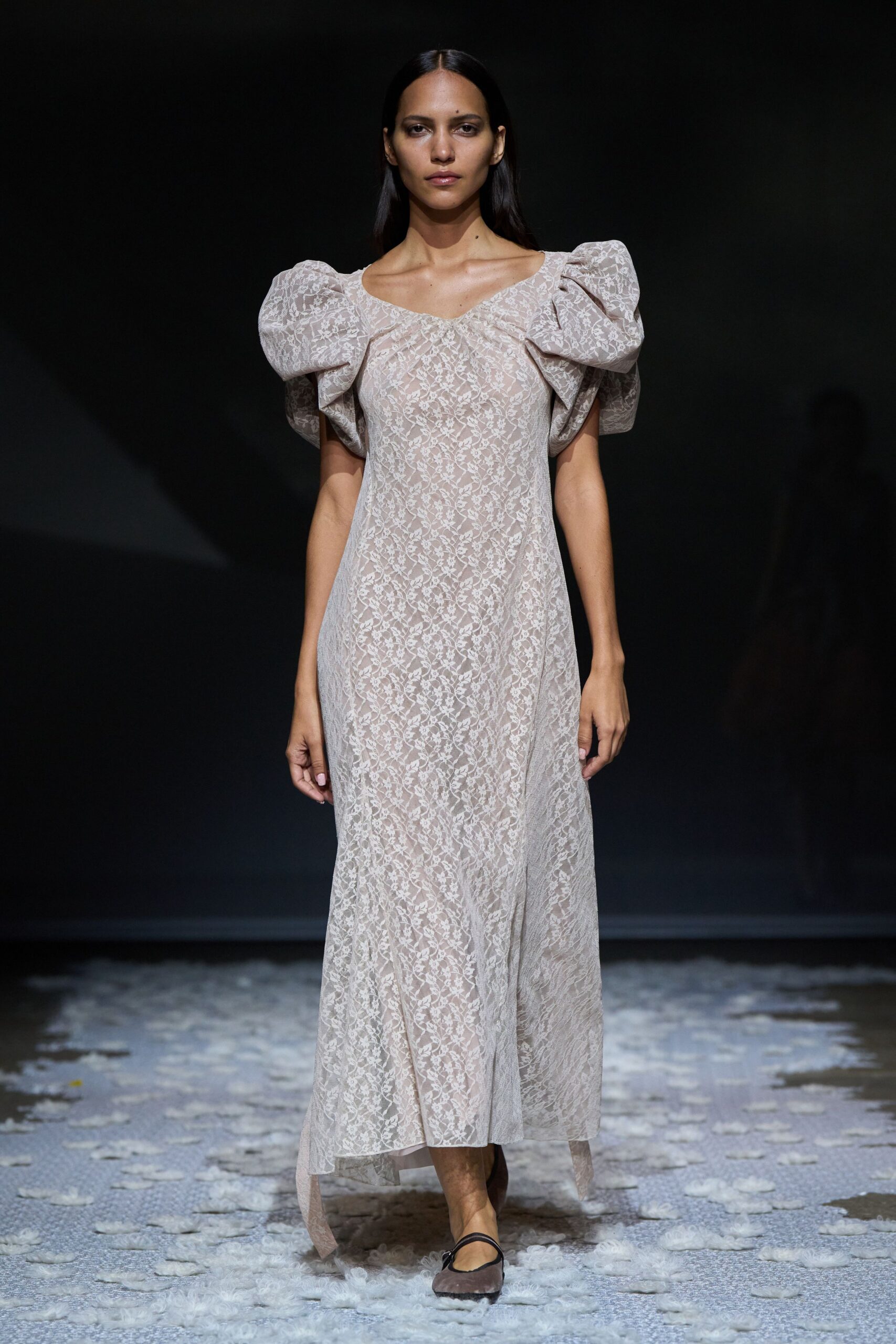 Blush floral lace dress with swollen puff sleeves and a handkerchief hem. Taupe mesh flats crossed with a narrow black instep strap. Morning after the wedding, carrying coffee across a damp hotel lawn.