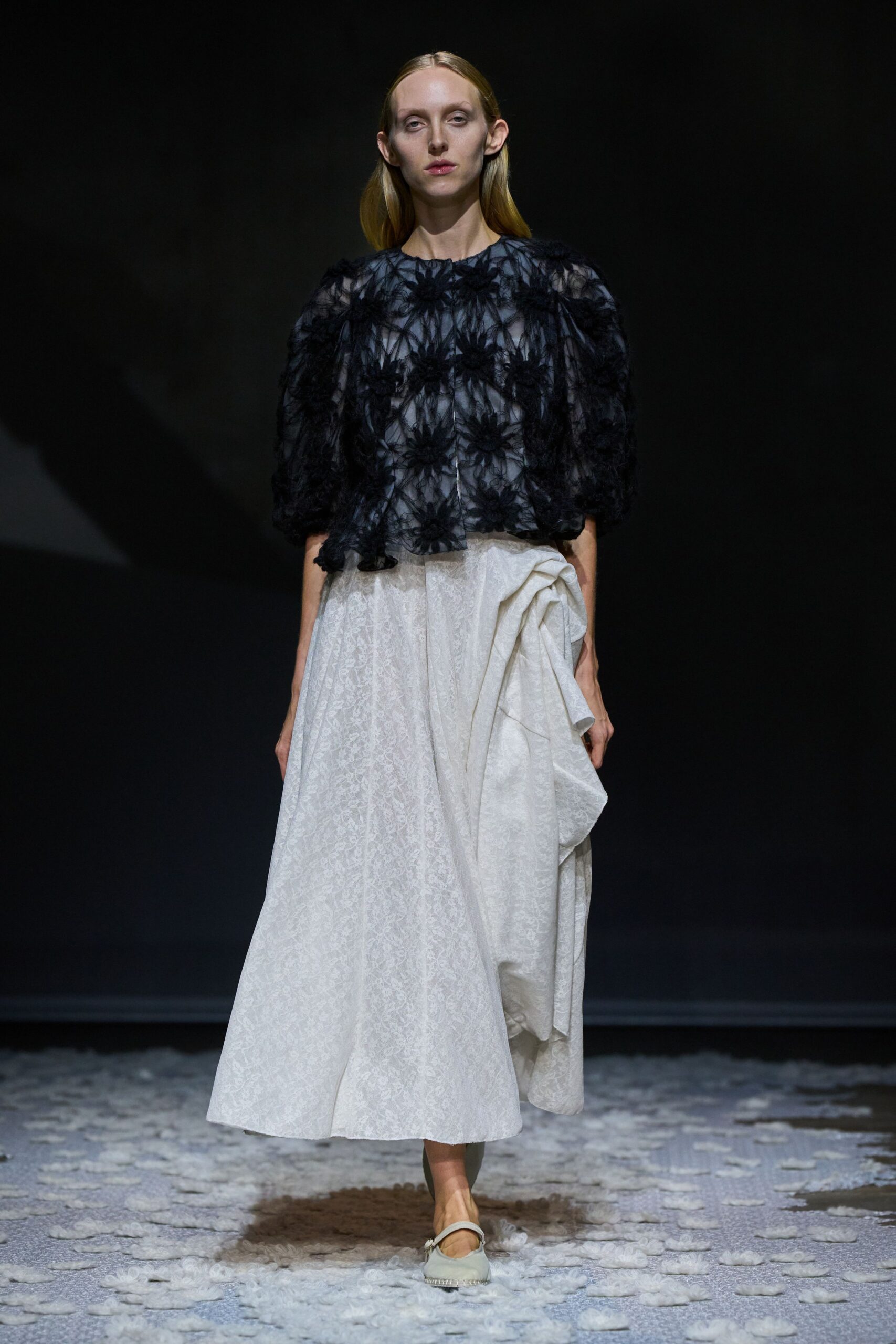 Sheer black organza top crowded with fuzzy appliqued flowers. Ivory jacquard midi skirt, one side hitched into a bundled swag. Pale Mary Jane flats with a pearl-fringed toe. Walking across a chapel aisle after the petals have started sticking to your shoes.