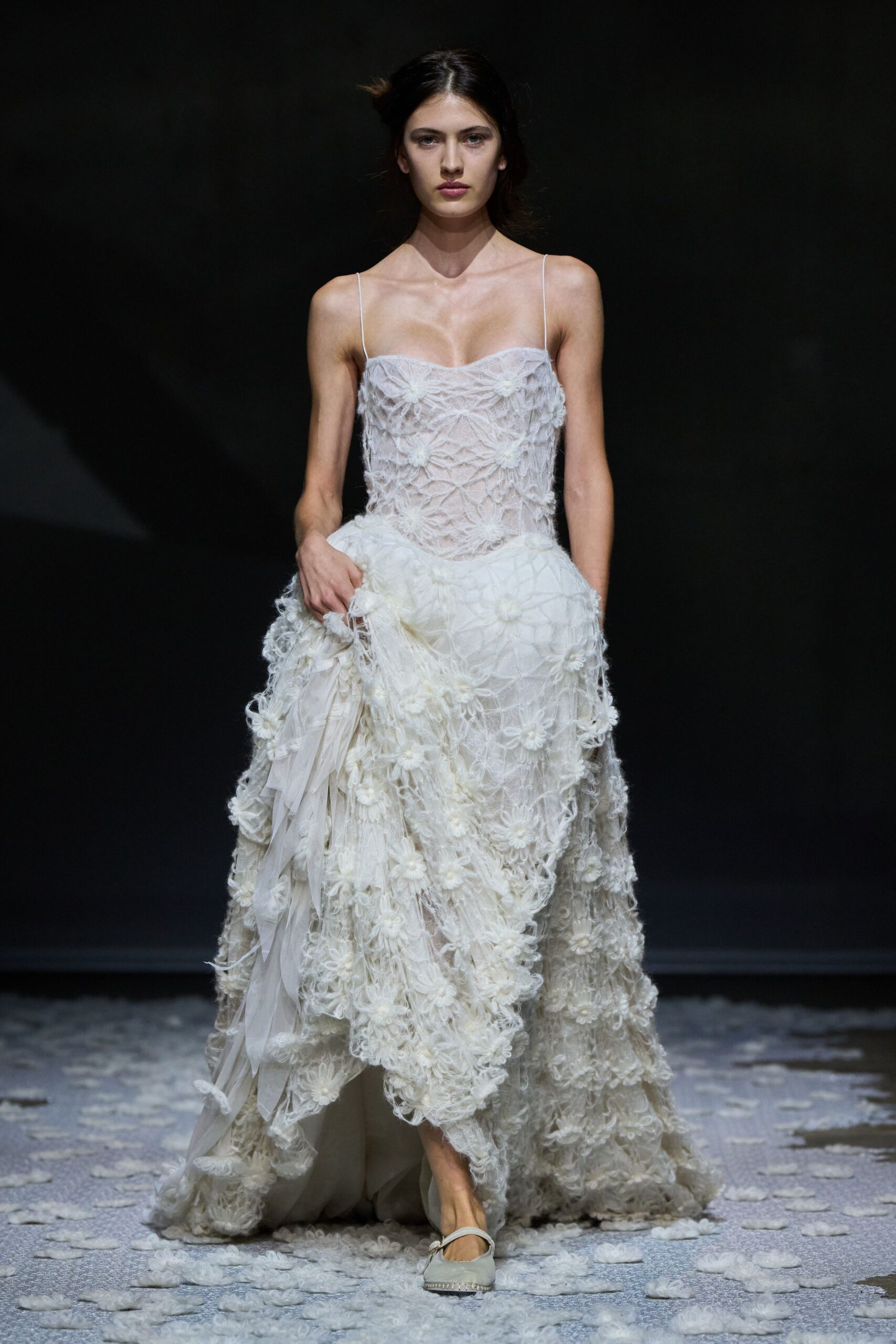 Ivory slip dress with webbed floral appliqué and a hand-lifted overskirt. Pale Mary Jane flats with braided jute edging at the sole. Crossing a chapel lawn after the chairs have been folded away.