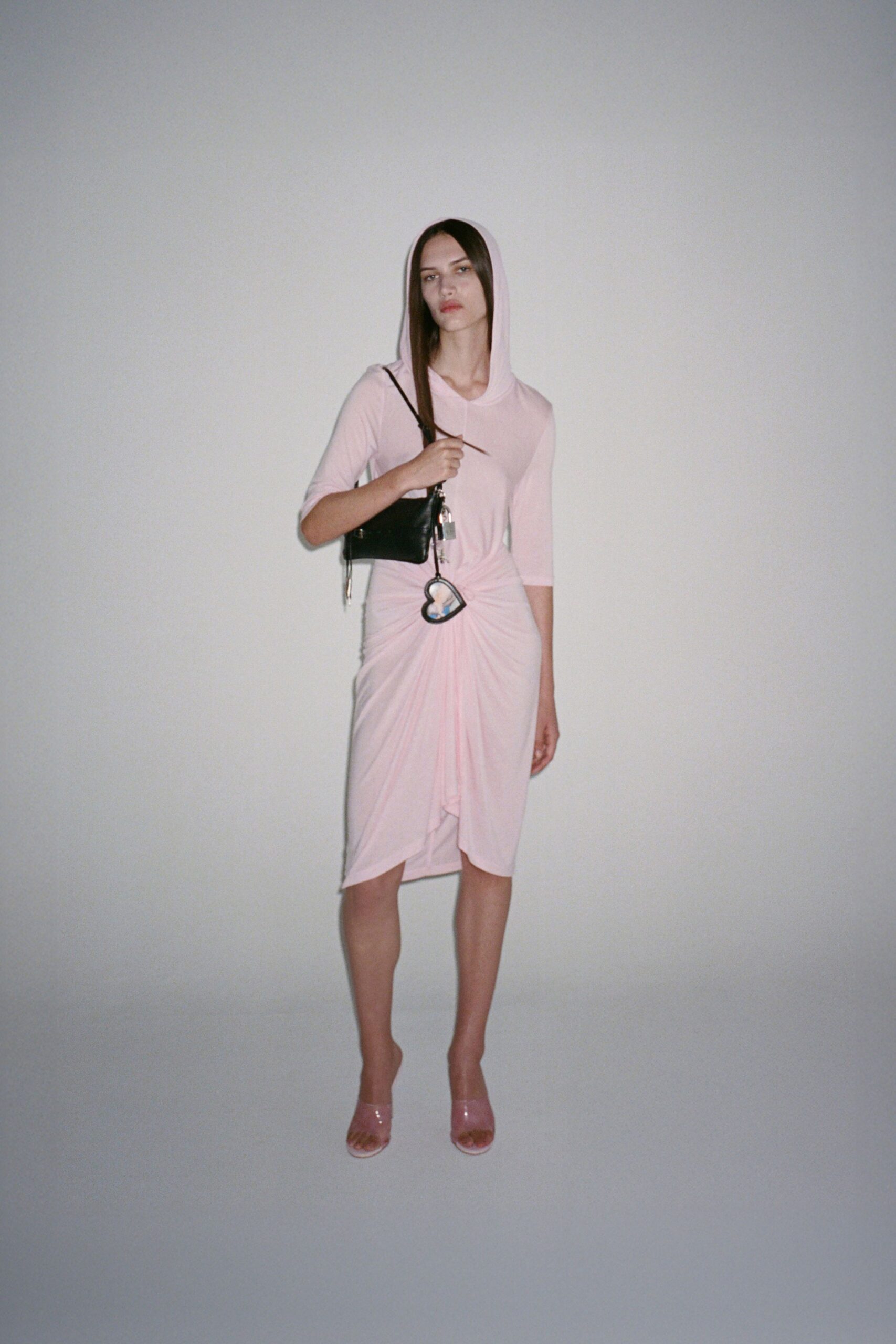Pale pink jersey dress with a soft hood and knotted drape. Black zip baguette with dangling silver padlock and heart charm. Glossy blush vinyl mules. For buying cold medicine at the corner shop after midnight.