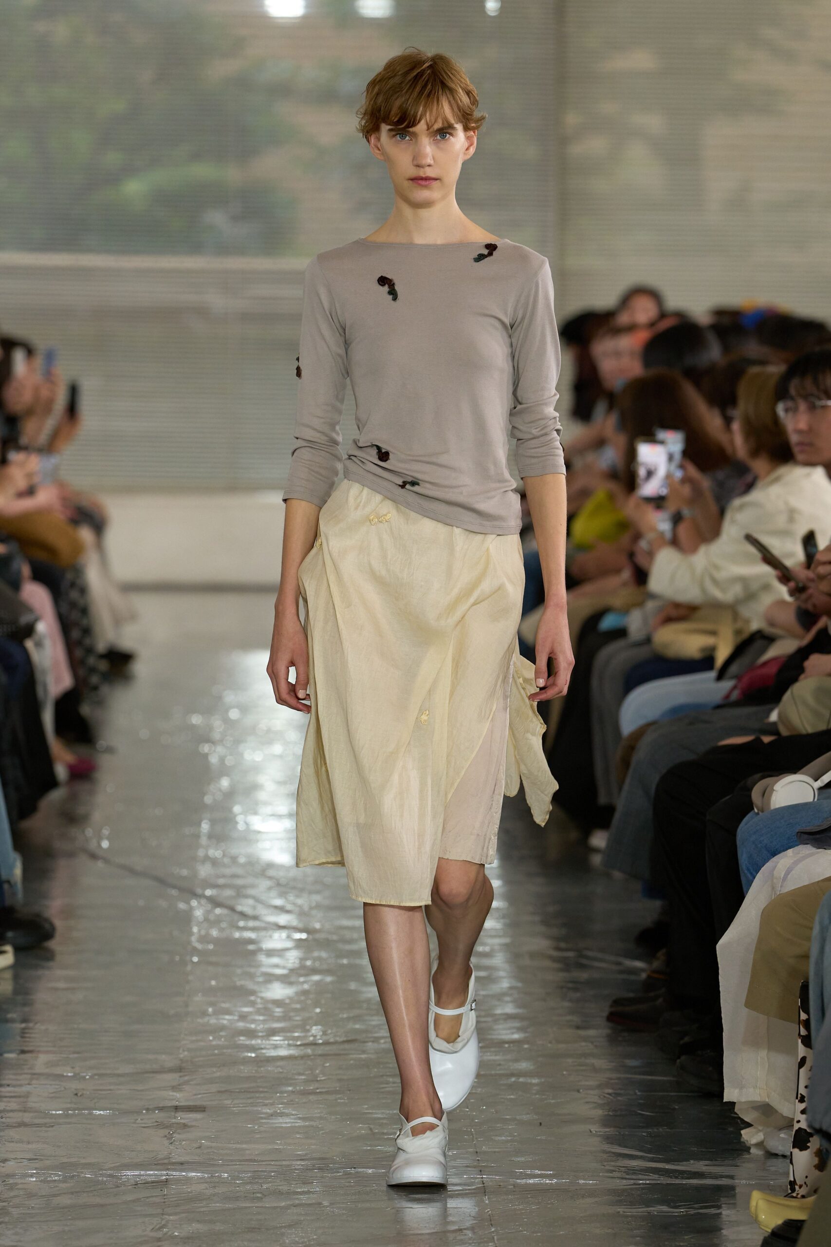 Dove grey jersey boatneck top, lightly ruched at the hip and dotted with tiny rosette appliques. Cream crinkled wrap skirt with a sheer underlayer peeking through the slit. White Mary Janes. Museum atrium, rain still drying on the floor.