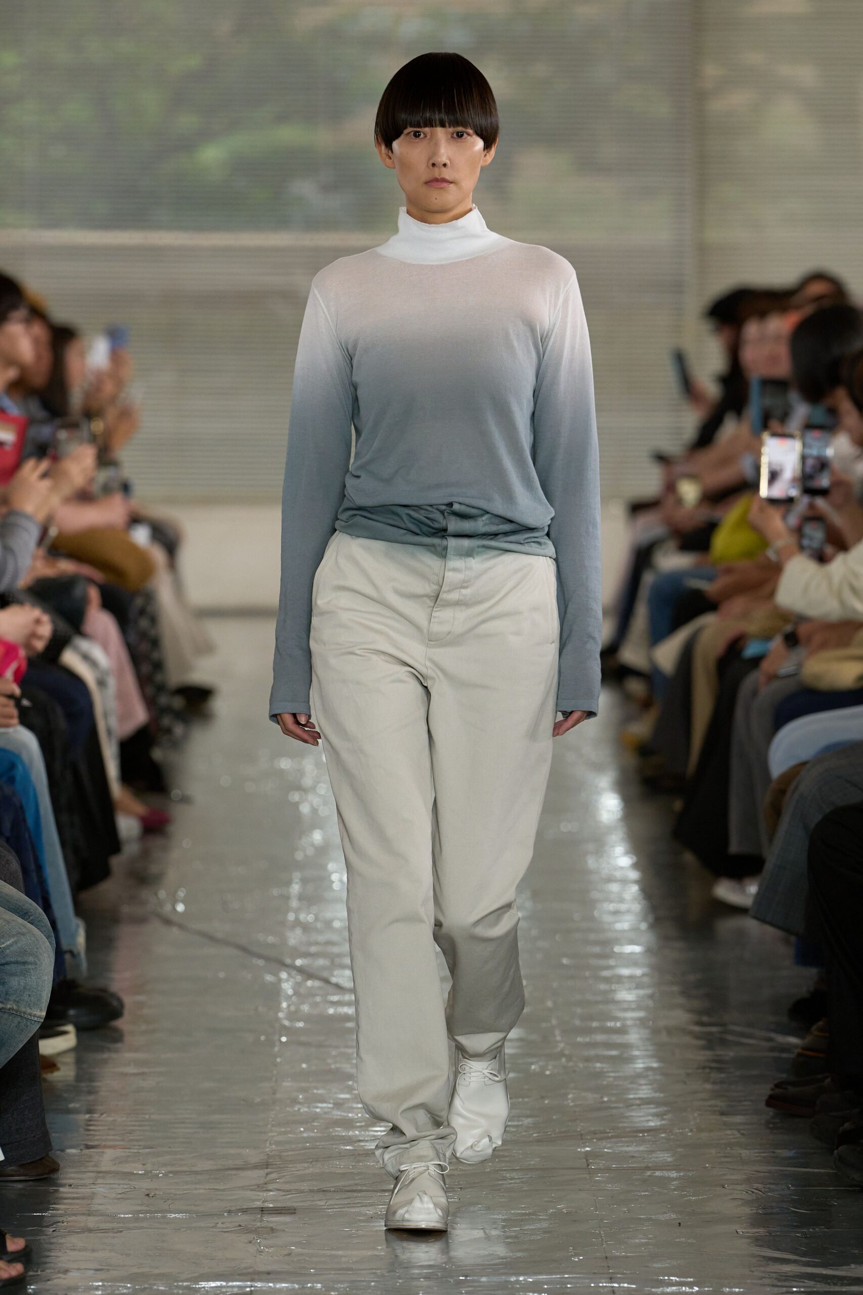 Sheer ombre jersey turtleneck fading from white to mist blue, hem twisted into the waistband. Chalk cotton trousers with a soft break over white leather lace-ups. Crossing a quiet atrium just after the rain stops.