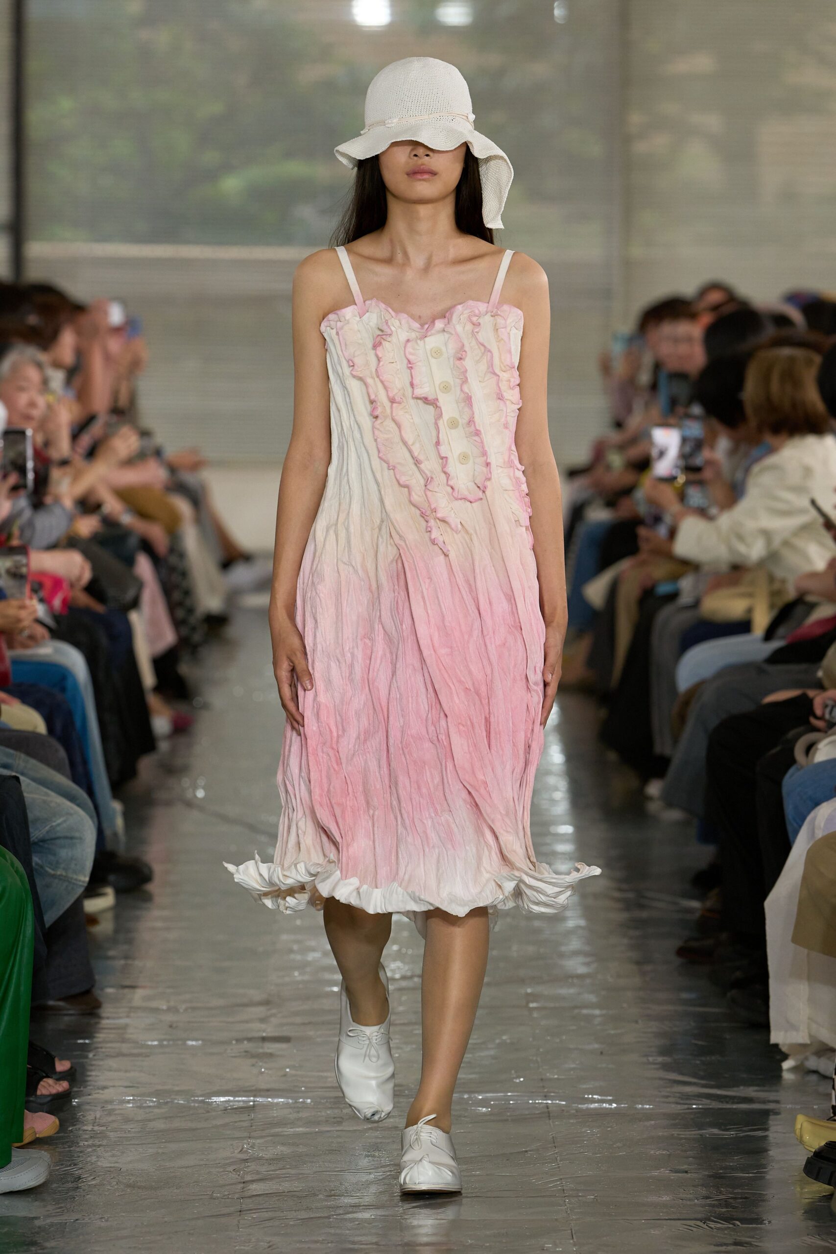 White open-weave sunhat with a drooping brim, slip dress in crinkled cotton washed from cream to shell pink, traced with ruffled seams and a row of pale buttons. White lace-up flats. On a veranda after rain, before the cake is cut.