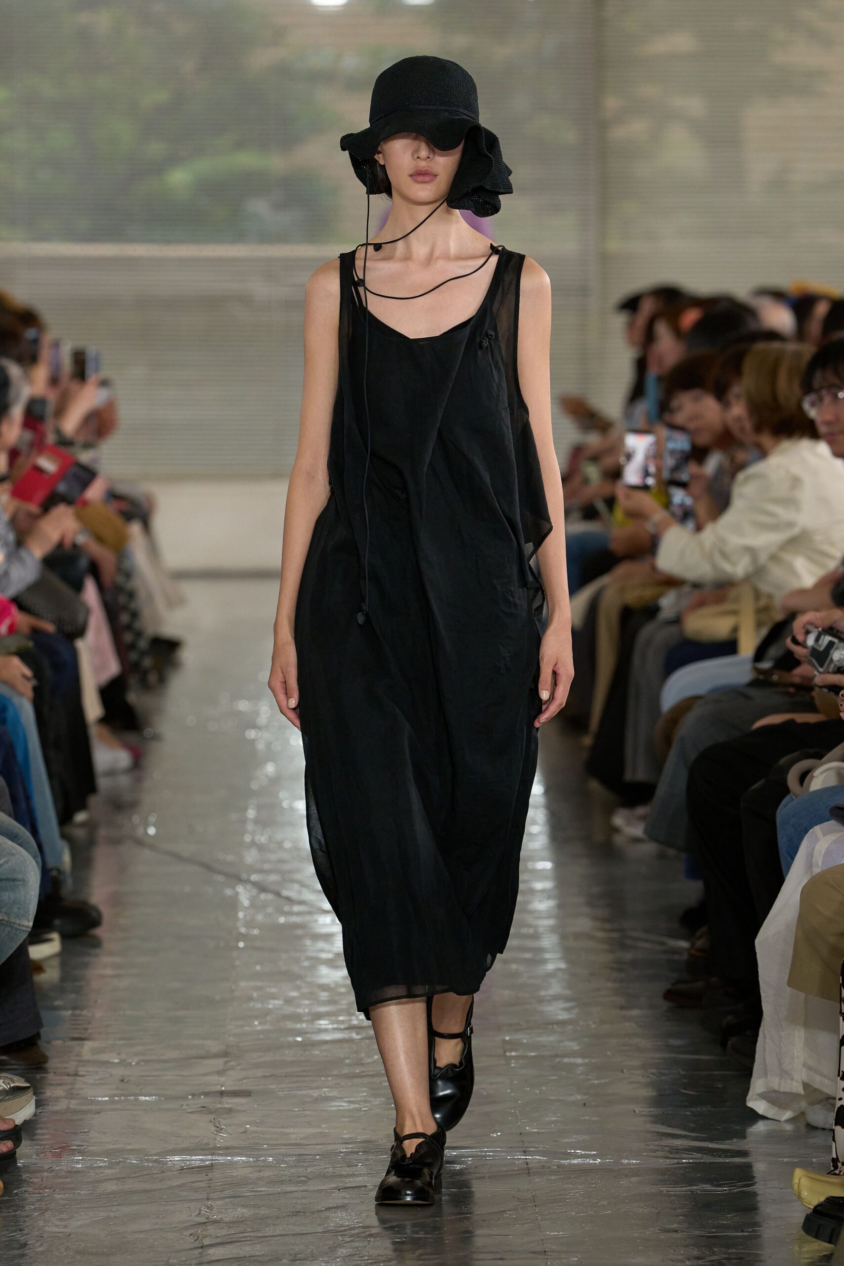 Black crinkled sunhat with a floppy brim and dangling cord, sheer black slip dress with a twisted front panel and raw-edged overlay, black leather Mary Janes. Like crossing a tiled bathhouse corridor just before closing.