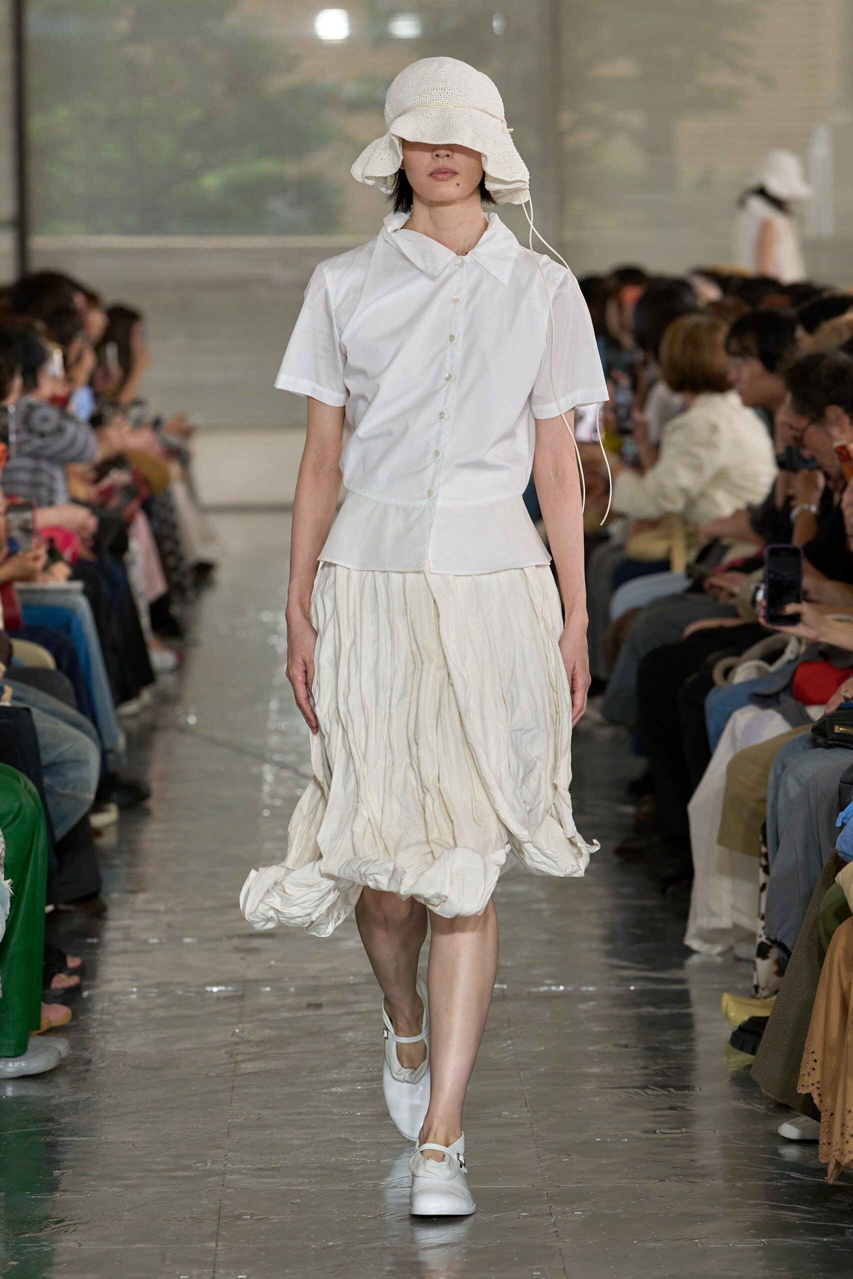 White woven sunhat with a floppy brim and trailing cord, white poplin short-sleeve shirt with a dropped peplum, crinkled cream skirt with a rolled hem, white Mary Jane flats. Late checkout at a quiet seaside pension.