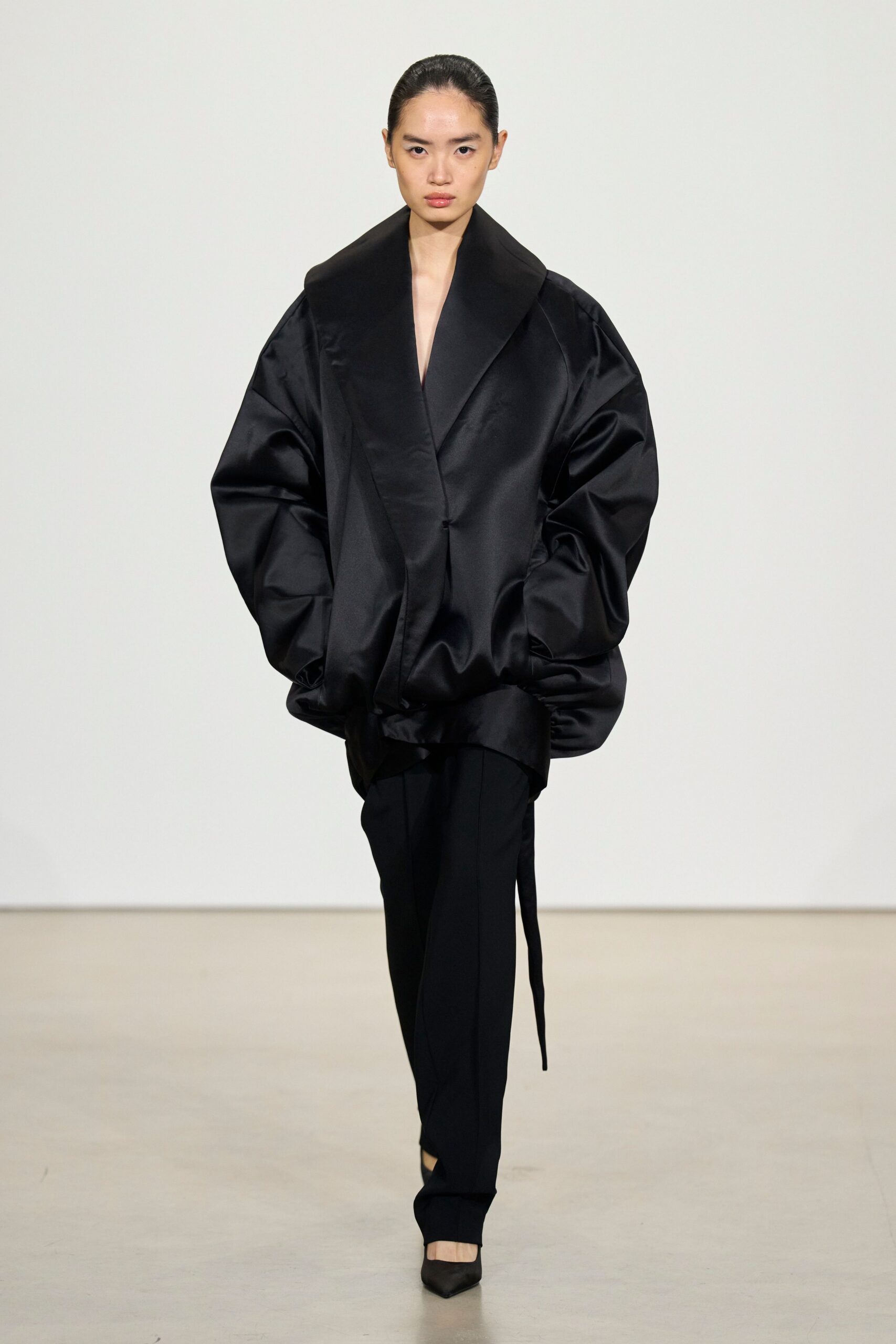 Black satin cocoon coat with a huge shawl collar and balloon sleeves. Slim black trousers with a pressed crease and one long hanging tab. Pointed black pumps. For crossing a museum atrium before the staff turn the lights down.