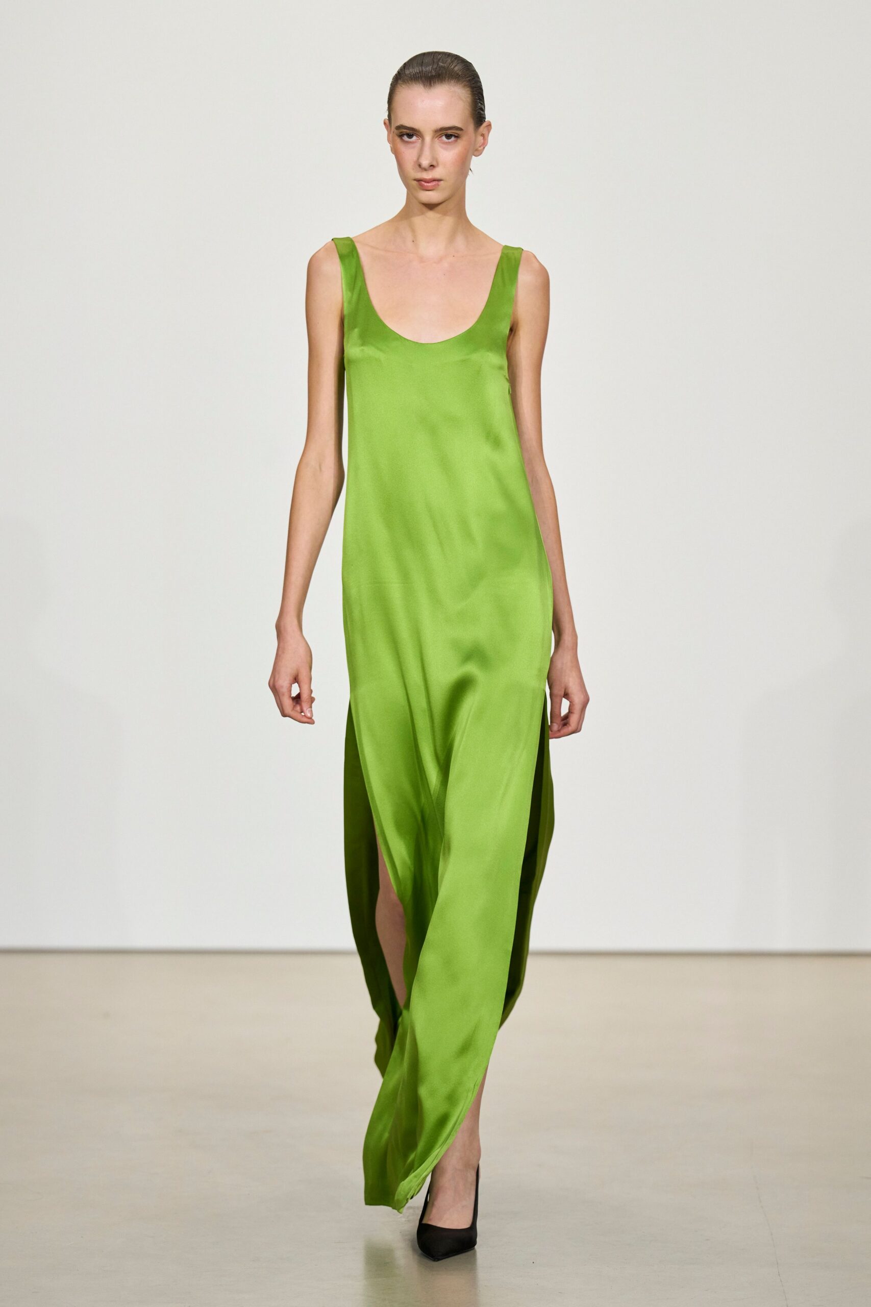 Acid-lime satin slip dress with a low scoop neck and thigh-high side slits. Black pointed pumps disappearing under the pooling hem. Crossing a hotel lobby at noon with lilies already opening.