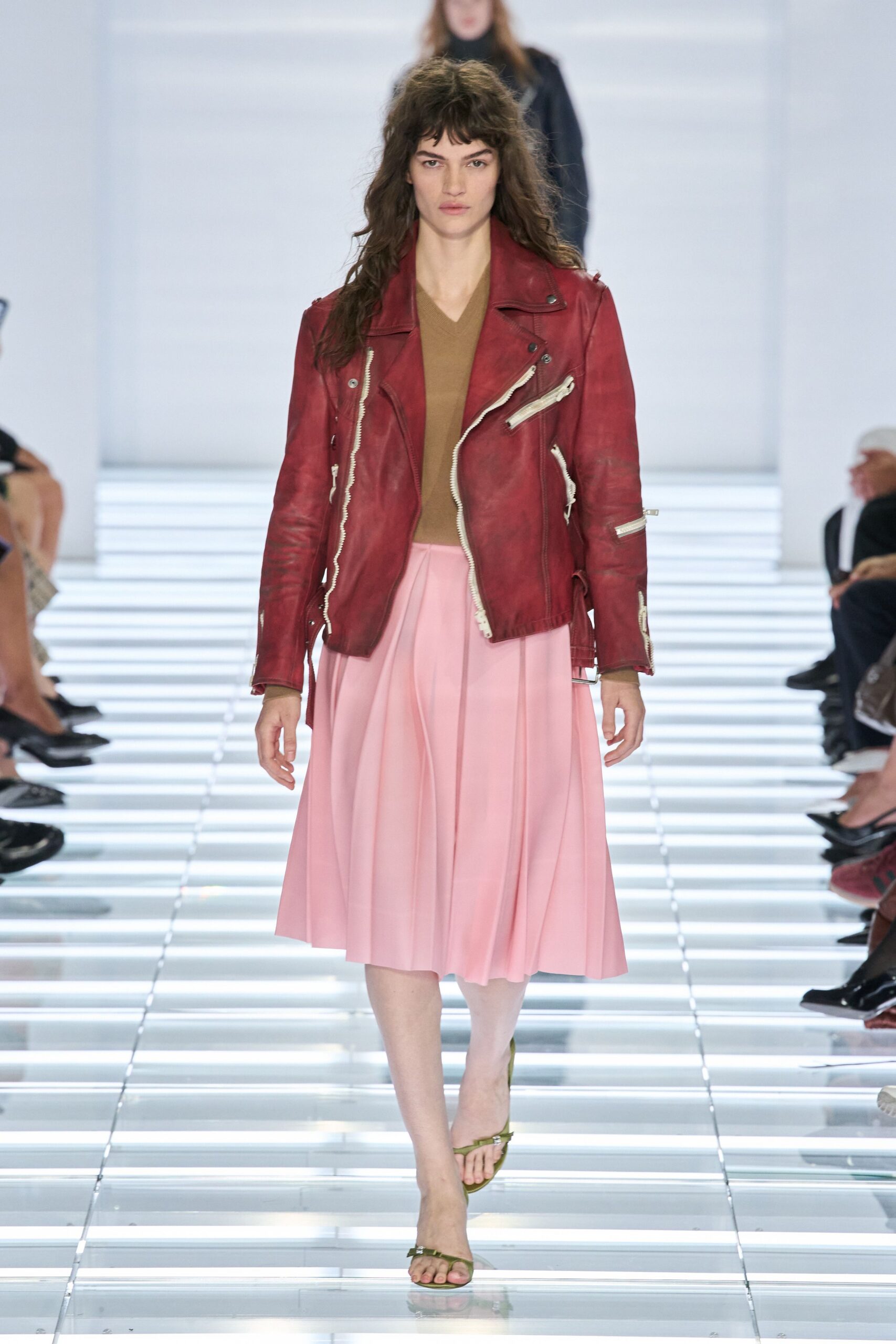Weathered oxblood leather biker jacket, chalky creases and thick white zips. Camel V-neck knit, cut close under the open lapels. Blush midi skirt in soft knife pleats that swing from the waist. Olive thong sandals with a small metallic glint at the toe. For buying flowers after rain, still wearing yesterday's jacket.