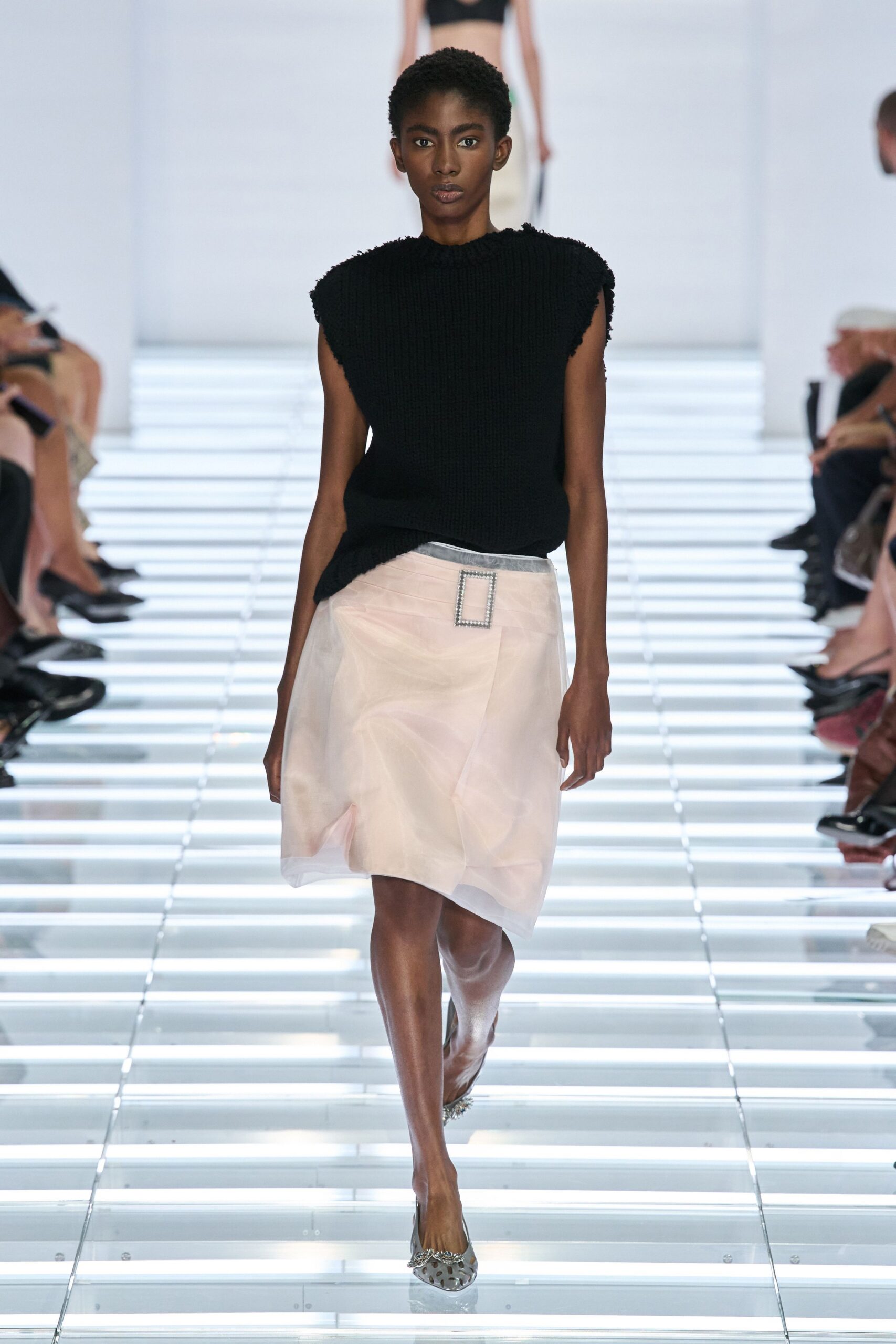 Black ribbed knit shell with fuzzy frayed cap edges. Blush sheer organza skirt, wrapped askew with a rhinestone buckle. Silver mesh pumps with crystal-cluster toes. Crossing the hotel atrium after a wedding, still holding the place card.