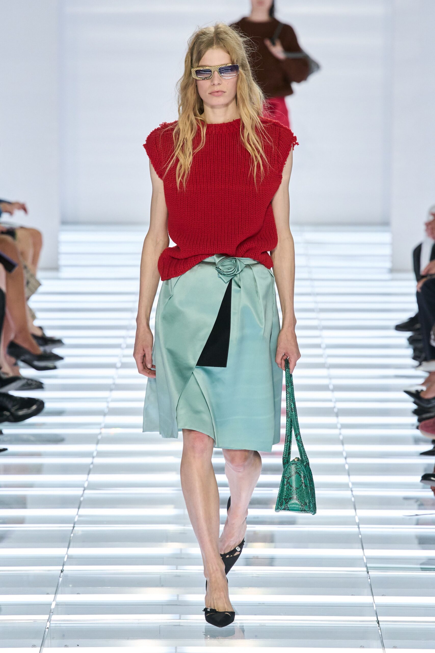 Square frames rimmed with rhinestones. Chunky tomato-red knit, armholes left raw and fuzzy. Seafoam satin wrap skirt pinned with a rosette knot. Green python shoulder bag. Black pointed flats with tiny bow hardware. Walking back from florist errands with wet pavement still bright.