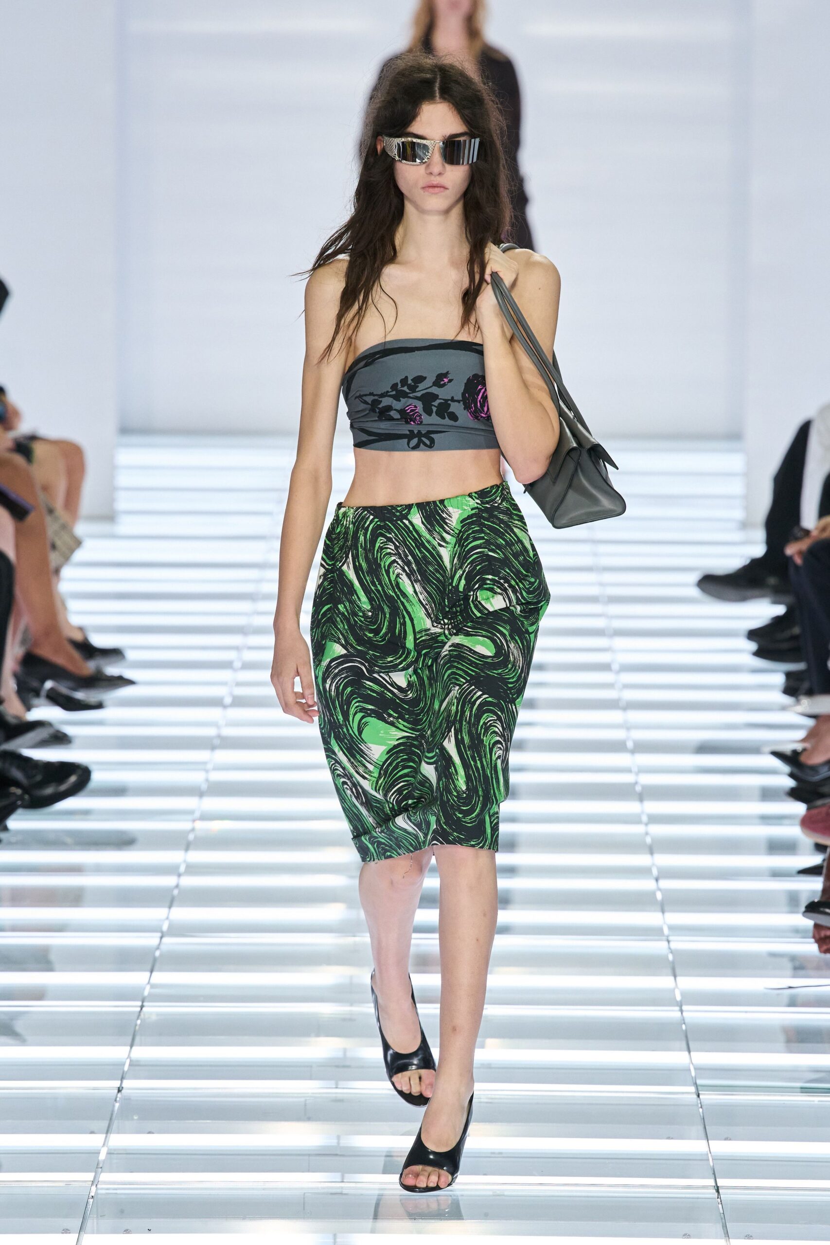 Mirror visor sunglasses with narrow striped reflections. Charcoal bandeau printed with black vines and bruised-purple roses. Knee-length pencil skirt in acid-green marbled jersey. Slate leather shoulder bag with long doubled straps. Black peep-toe heels. Walking into a nail salon just before the summer storm breaks.
