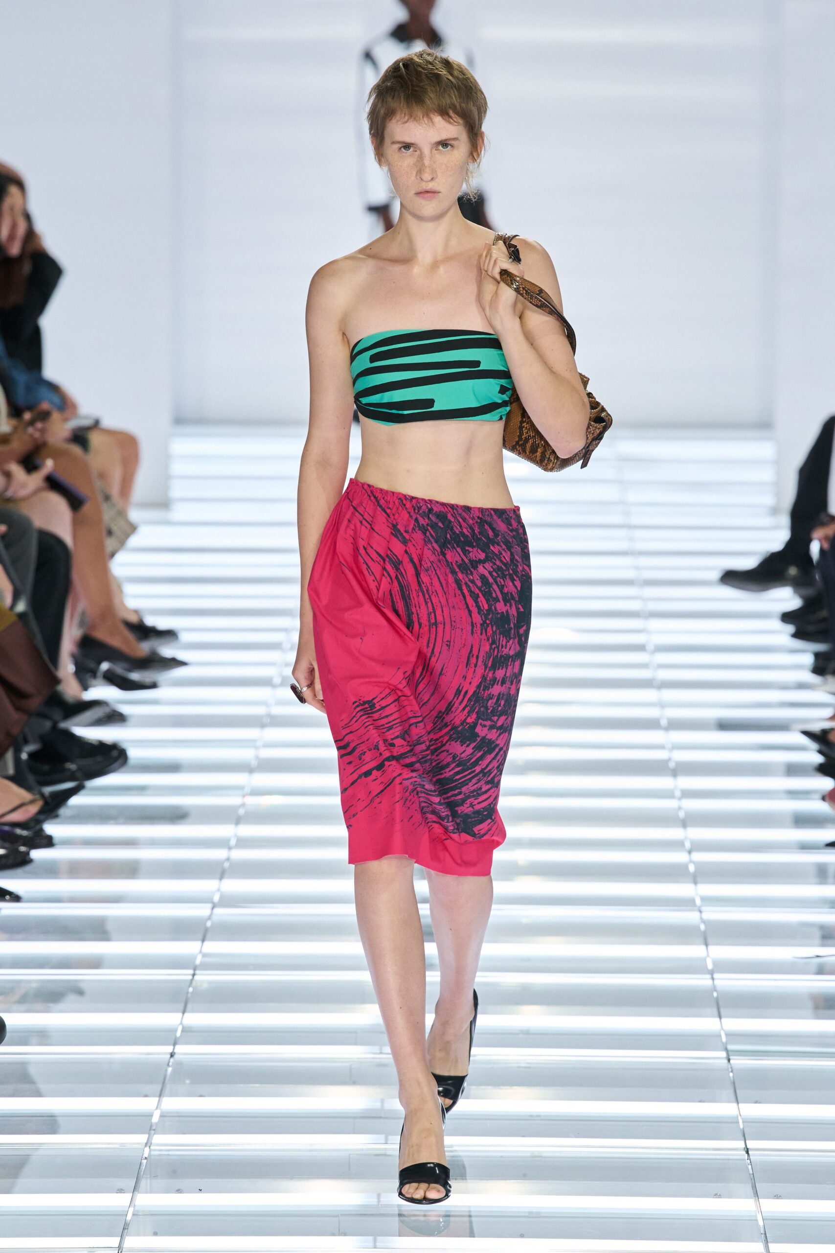 Turquoise stretch bandeau striped with thick black brushstroke bands. Brown python shoulder bag tucked high under one arm. Hot-pink pencil skirt with a black marbled whirl crossing the hip. Black patent mule sandals. Walking out for cold noodles with a beach towel still damp at home.
