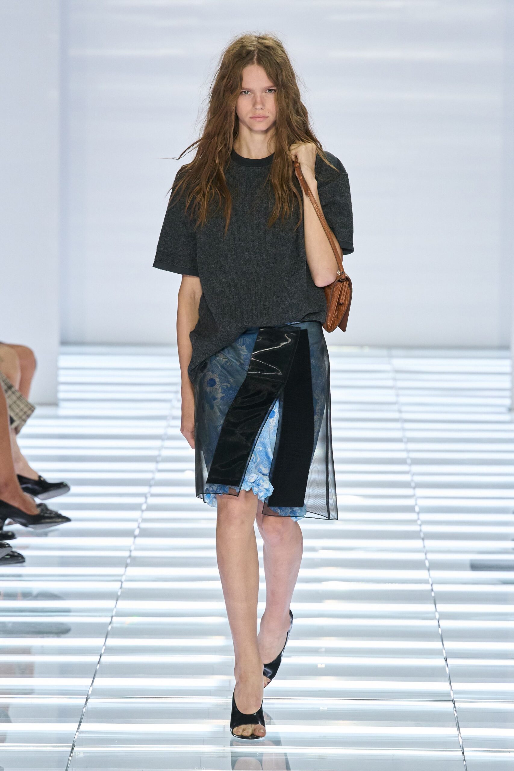 Charcoal ribbed knit tee, cut wide with dropped half sleeves. Asymmetric skirt layered in smoky organza, patent black panel over blue floral underlay. Tan croc-embossed shoulder bag with a narrow strap. Black peep-toe mules. Walking into a quiet office on Monday with last night's flowers still in the tote.