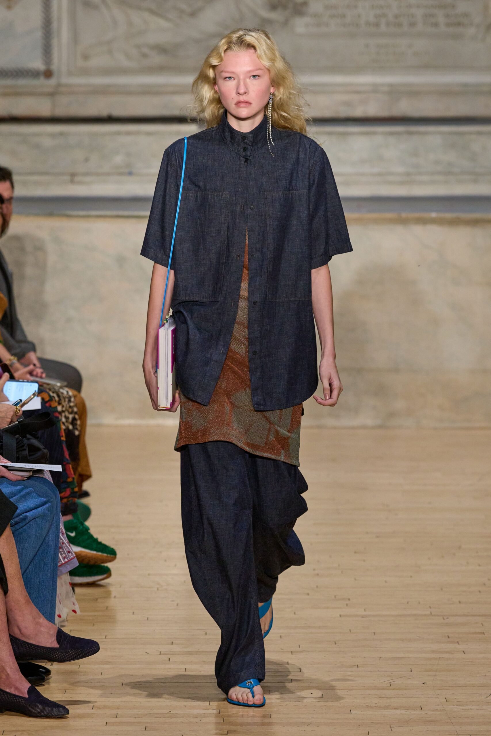 Dark indigo chambray shirt, high stand collar and rounded hem. Rusty sheer knit slip, mottled like oxidized metal. Loose indigo trousers pooling into soft folds at the ankle. Hardback book carried as a bag on a bright blue strap. Electric blue thong sandals. Walking into the library courtyard with three books due today.