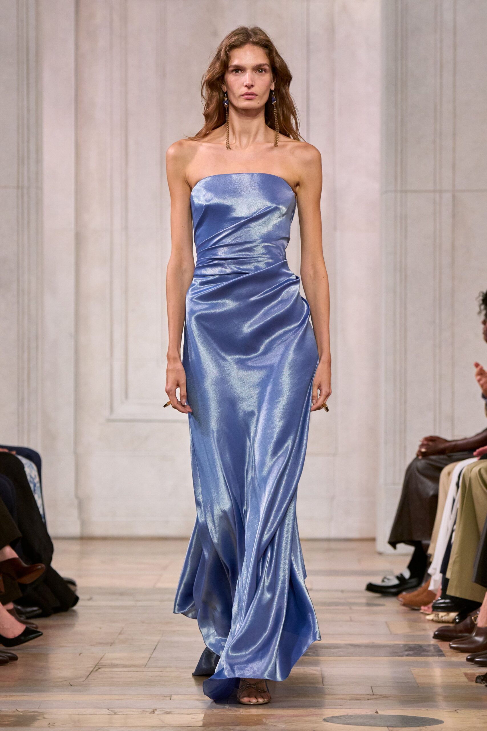 Strapless periwinkle satin gown, ruched through the waist and pooling at the hem. Long chain-drop earrings with dark blue stones at the lobe. Barely there brown sandals peeking from the draped front. For the wedding toast that drifts onto the hotel terrace after midnight.