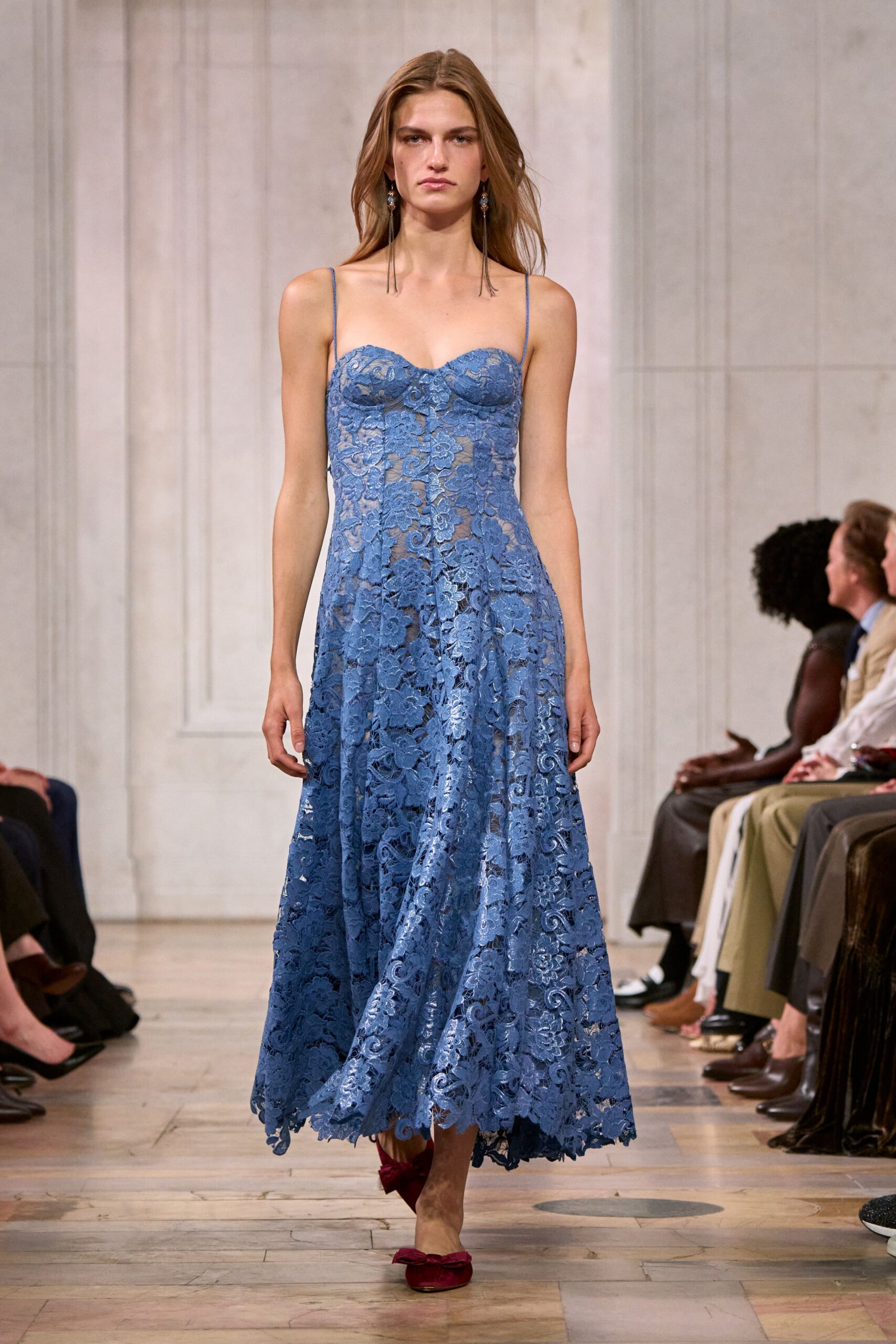 Long tassel earrings with tiny blue clustered stones at the lobe. Cornflower cord-lace slip dress, sweetheart cups and a scalloped hem swinging unevenly. Crushed wine velvet flats topped with bow knots. Garden wedding reception after the sun drops, grass already cooling underfoot.