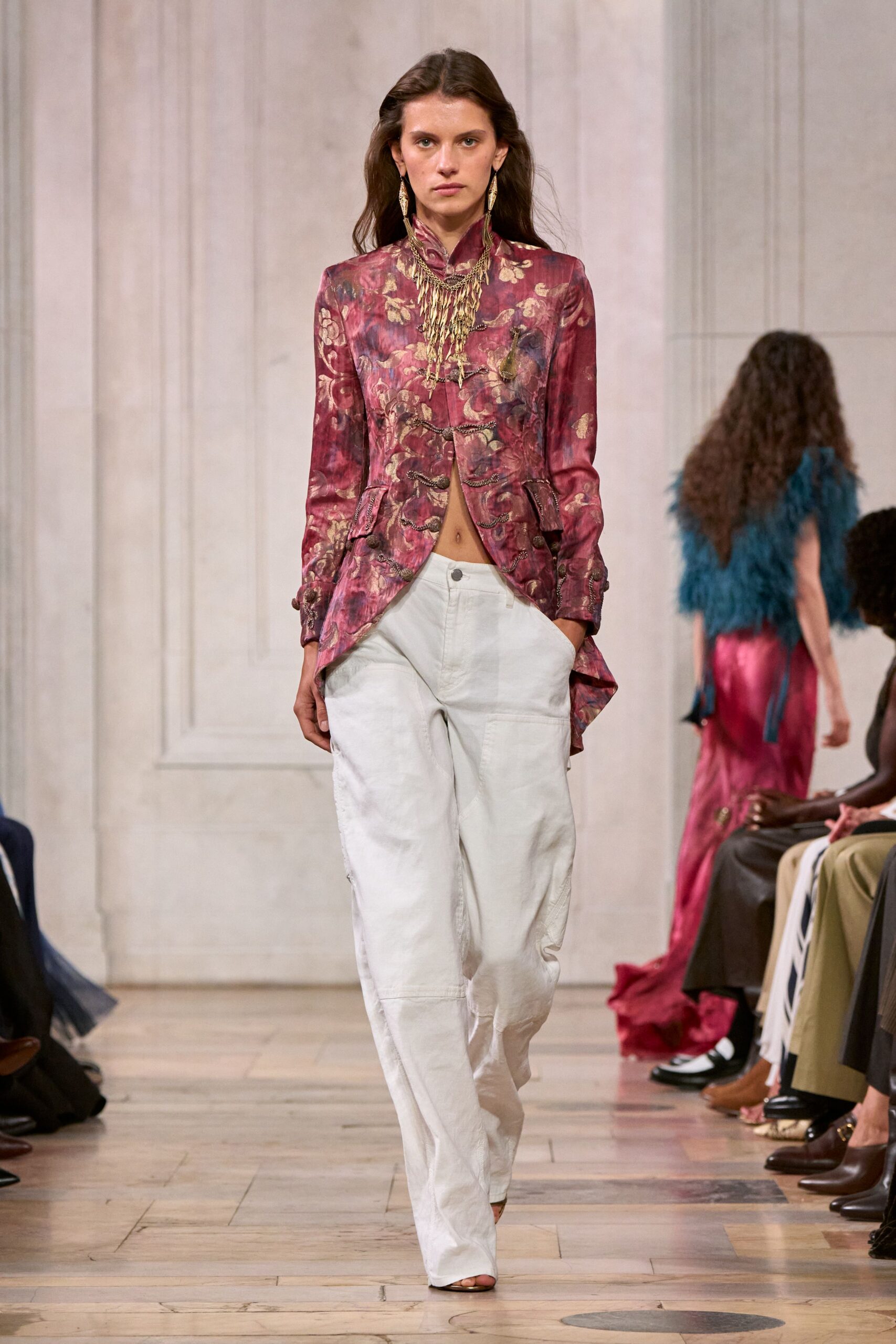 Layered brass fringe necklace, chains tangling into a narrow bib. Burgundy floral brocade jacket with frog closures and a split curved hem. Chalk wide-leg trousers, workwear seams bending around the knee. Barely there toe-baring sandals. For drifting through a faded seaside hotel after the wedding crowd has gone.